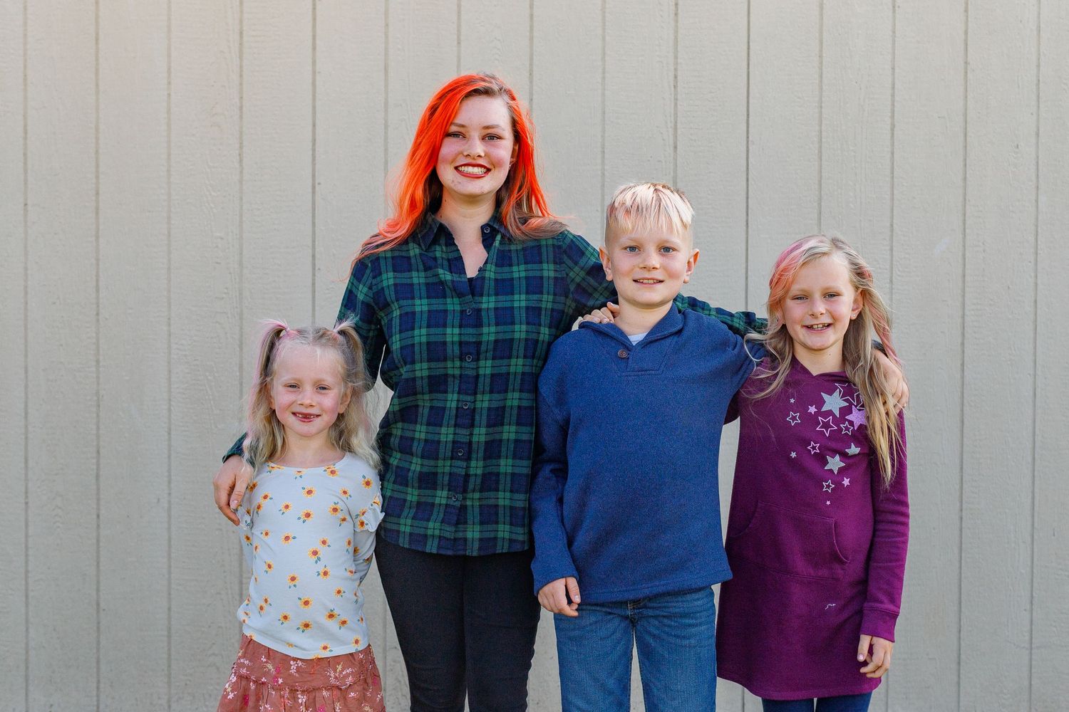 A group of people wearing casual clothing stand together and smile against a gray wall background.