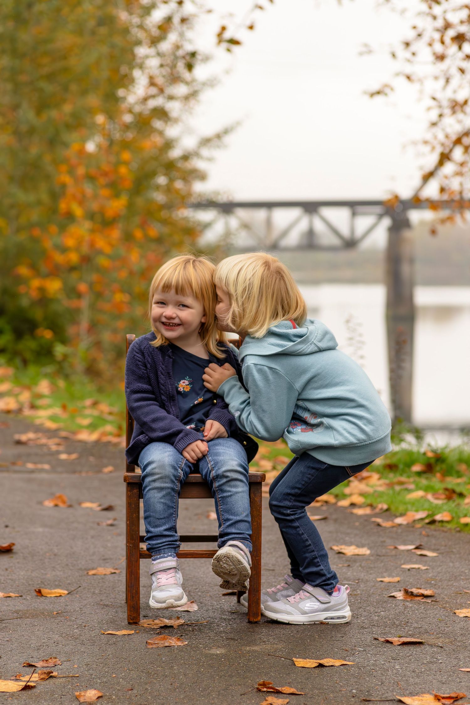 Two children sharing sweet moments while playing on wooden benches surrounded by autumn leaves.