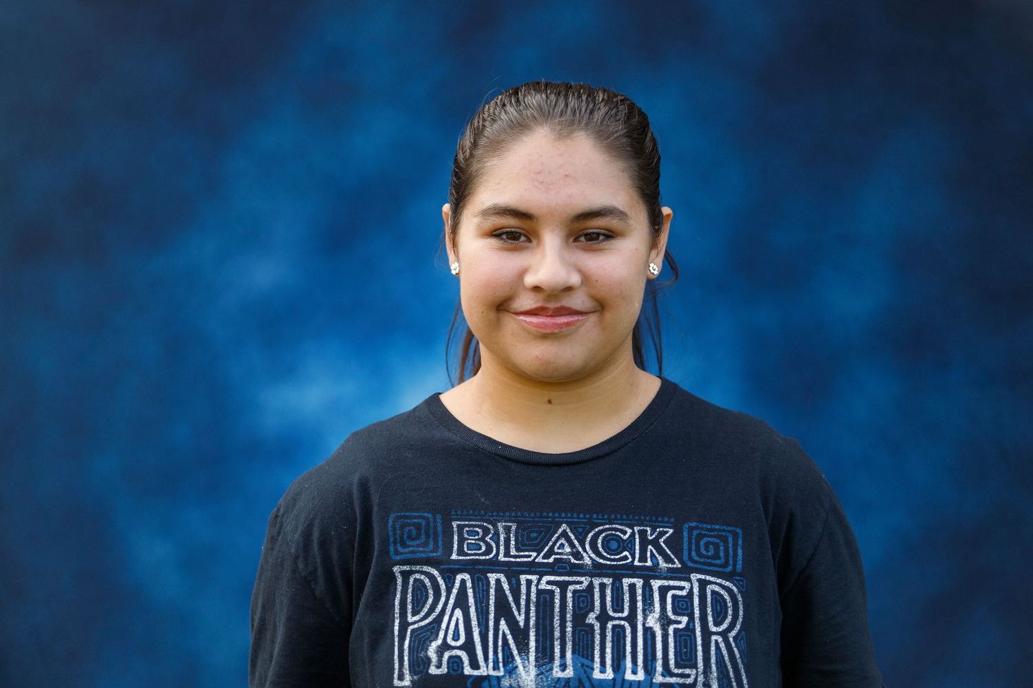 Person in a black Black Panther t-shirt smiling against a blue mottled background.