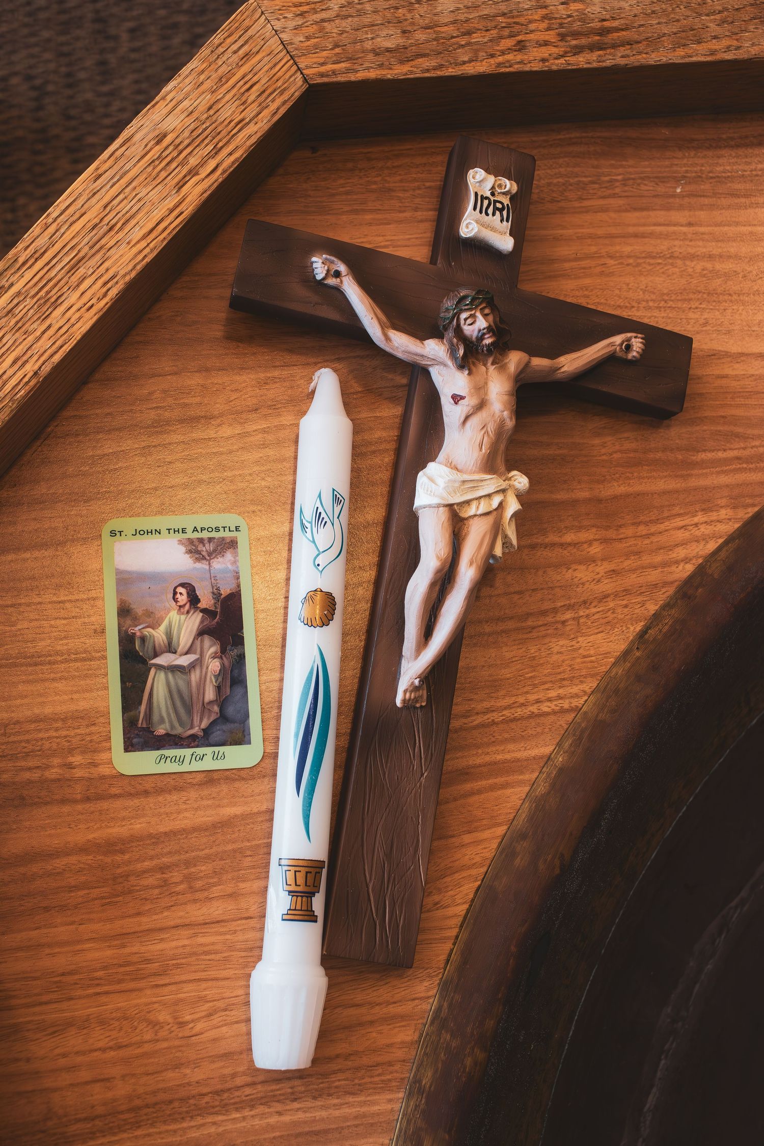 Religious items including a wooden crucifix, prayer card, and decorative white candle arranged on a wooden surface.