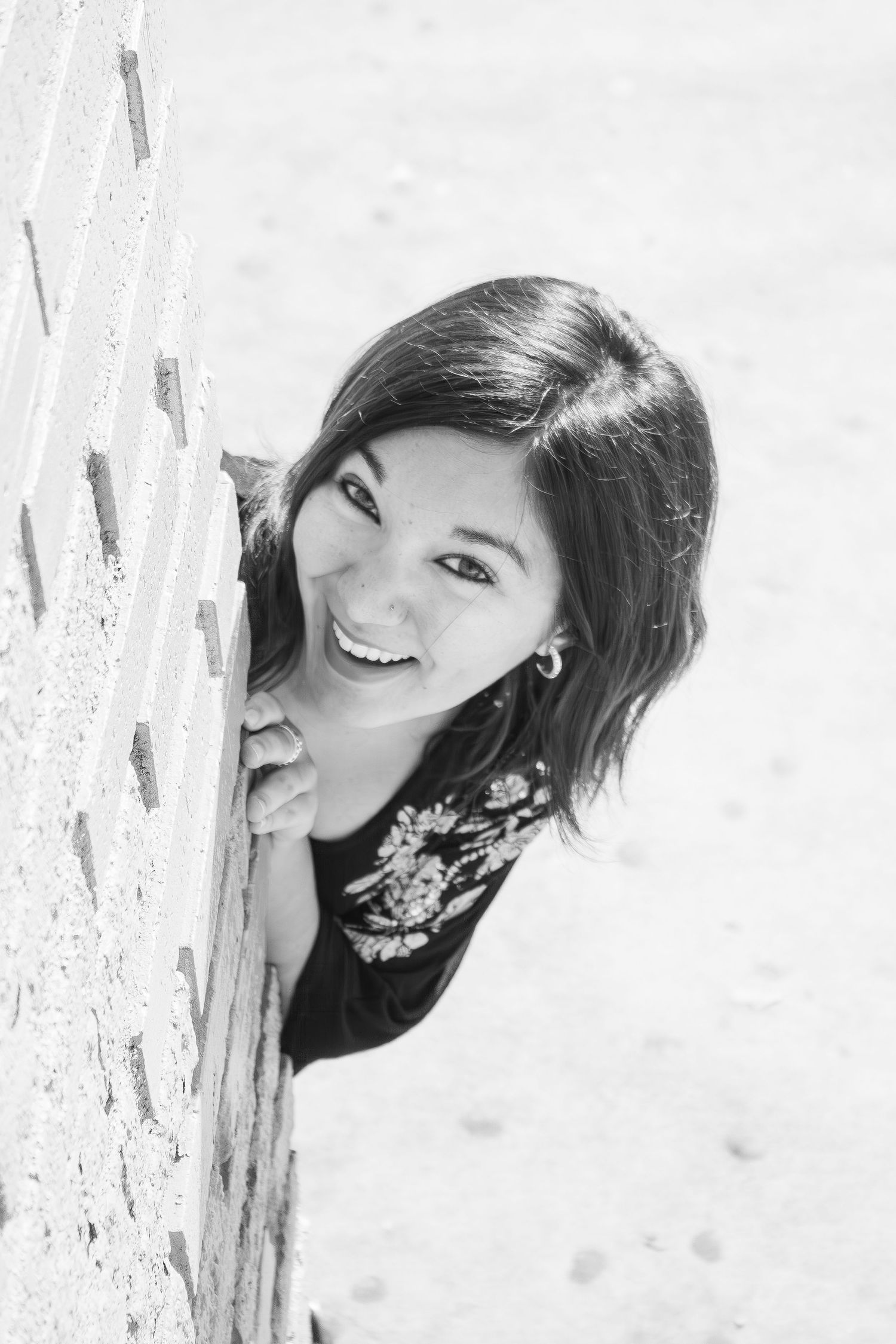 Black and white portrait of someone peeking around a corner with a bright genuine smile and wearing a floral top.