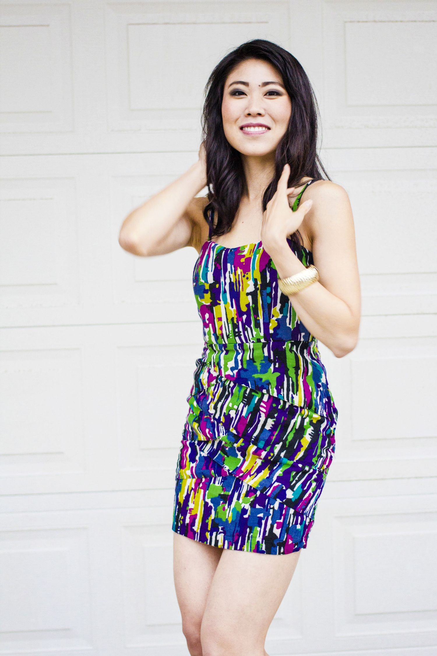 Person in a colorful abstract print mini dress poses playfully against a white garage door.