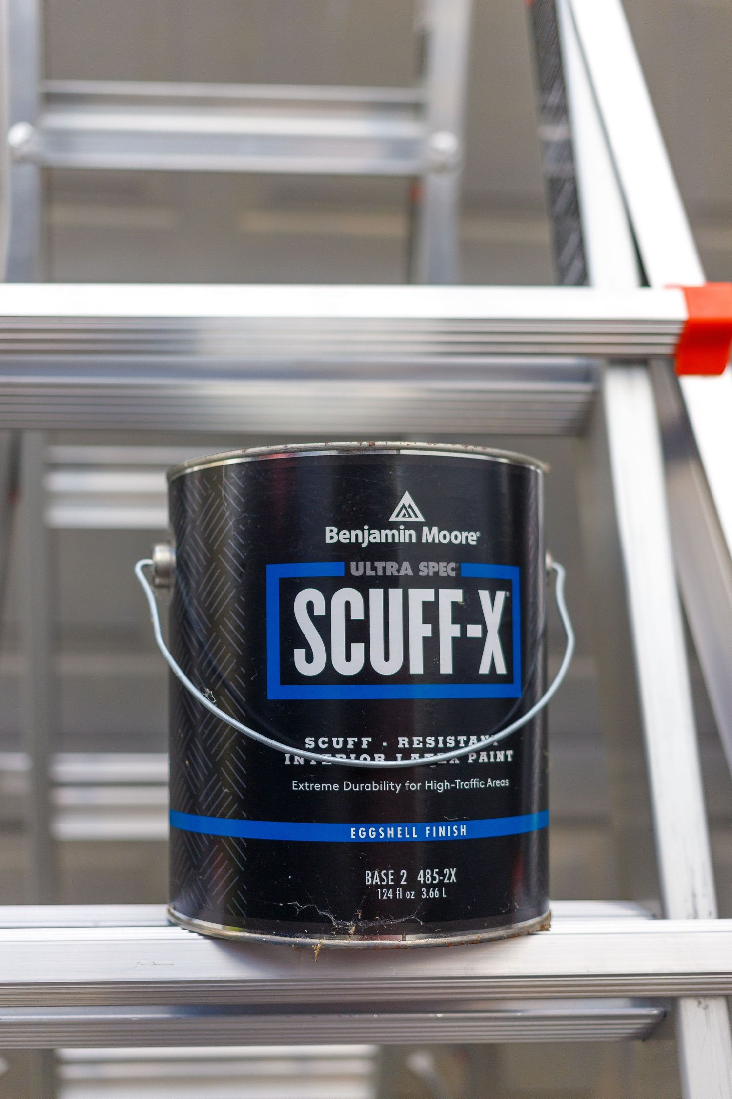 Close-up views of Benjamin Moore Scuff-X paint cans sitting on metal shelves show the product labeling and packaging.