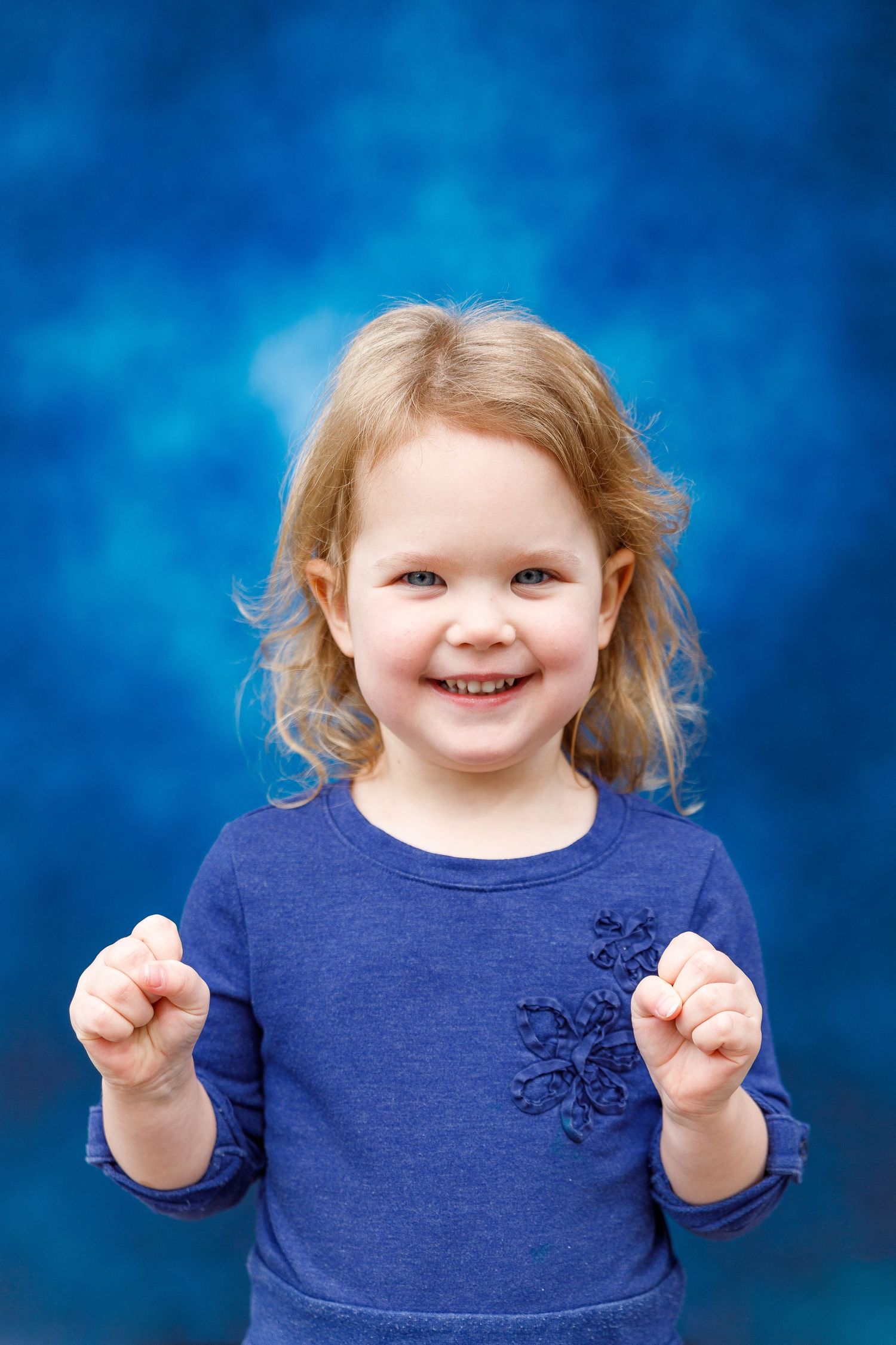 Young child wearing navy blue sweater with snowflake detail smiles joyfully against bright blue background.