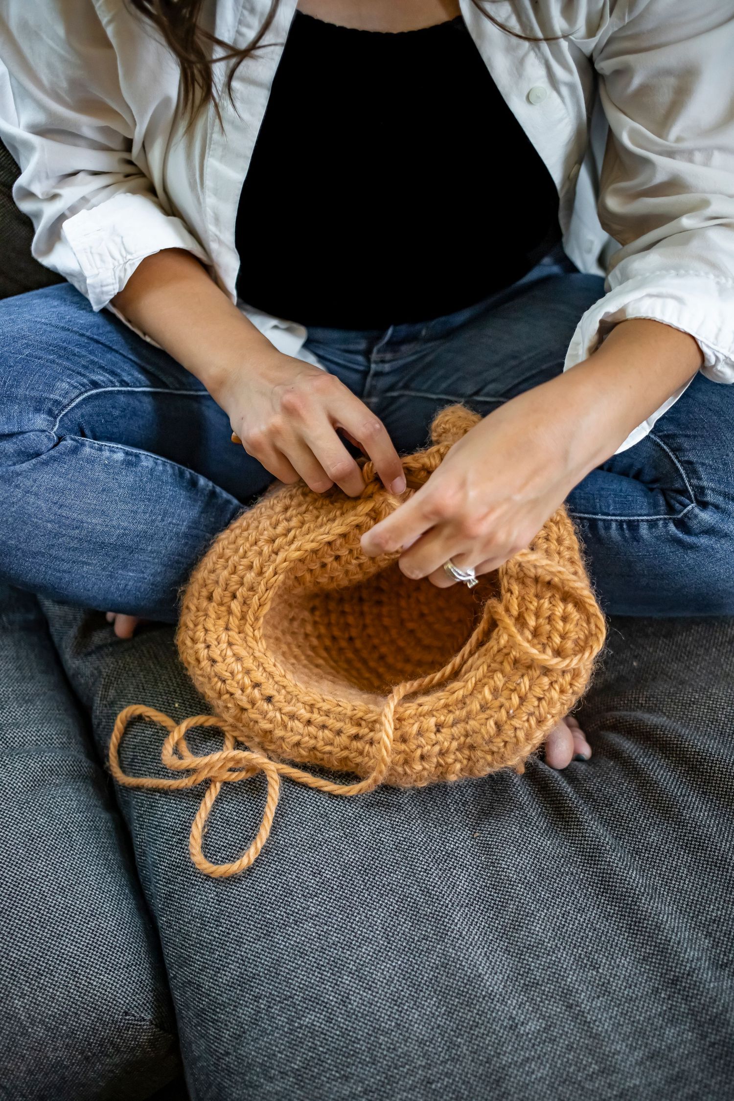 Close-up shot showing hands crocheting a round beige project with yarn against a grey background.