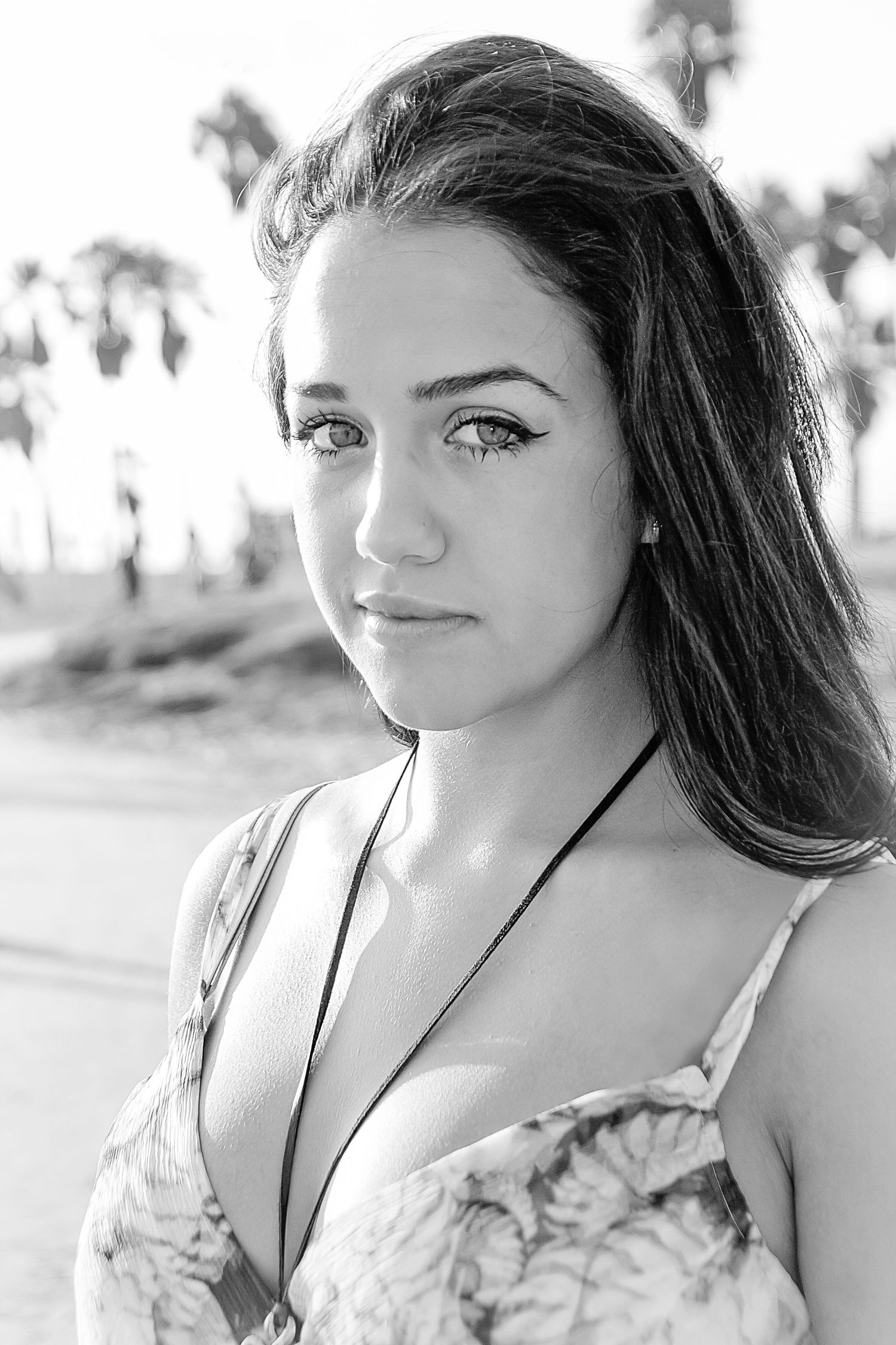 A black and white portrait features a young model in a floral dress against a palm tree background.