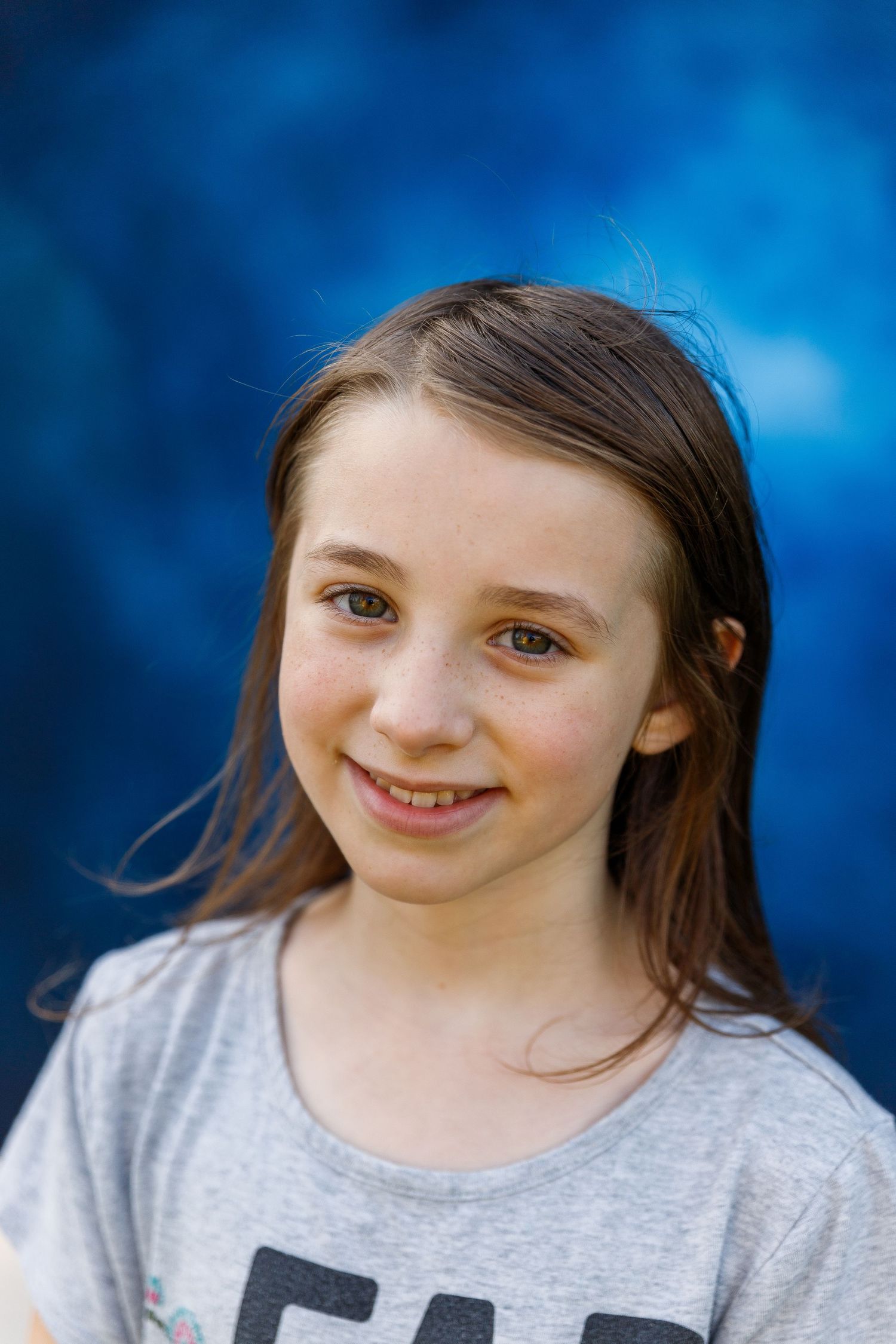 Portrait of a young person in a gray t-shirt smiling warmly against a blurred blue background.