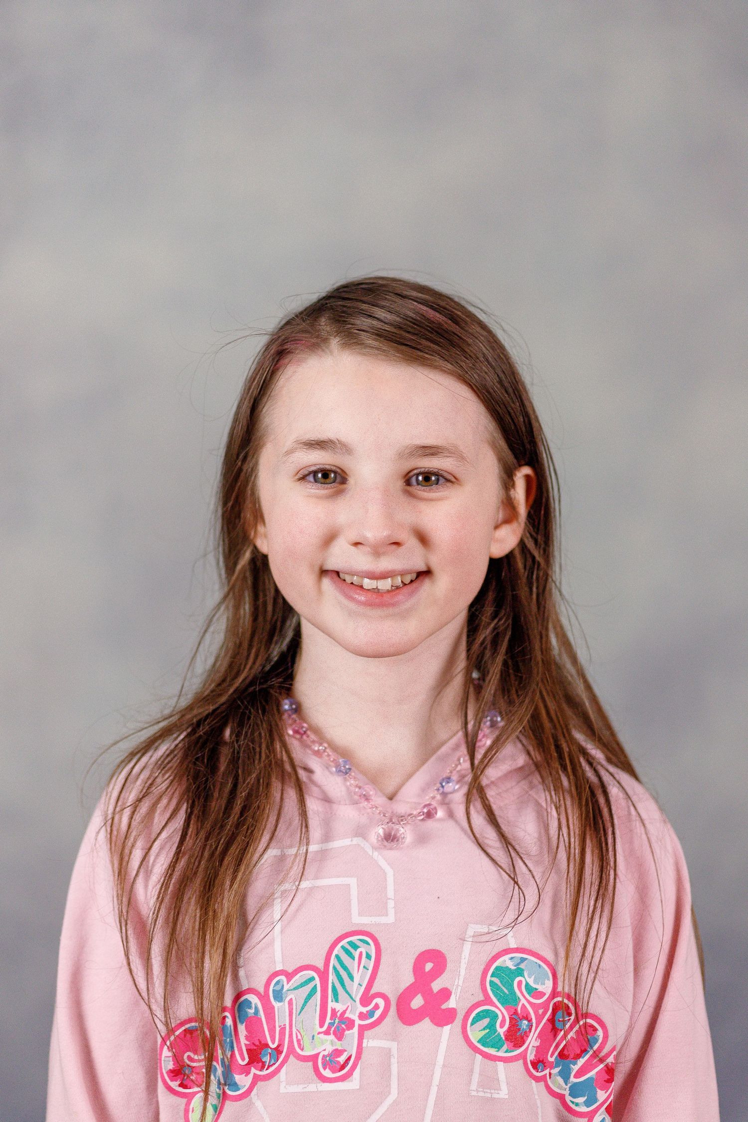 A portrait of a child wearing a pink sweatshirt with decorative text design against a gray background.