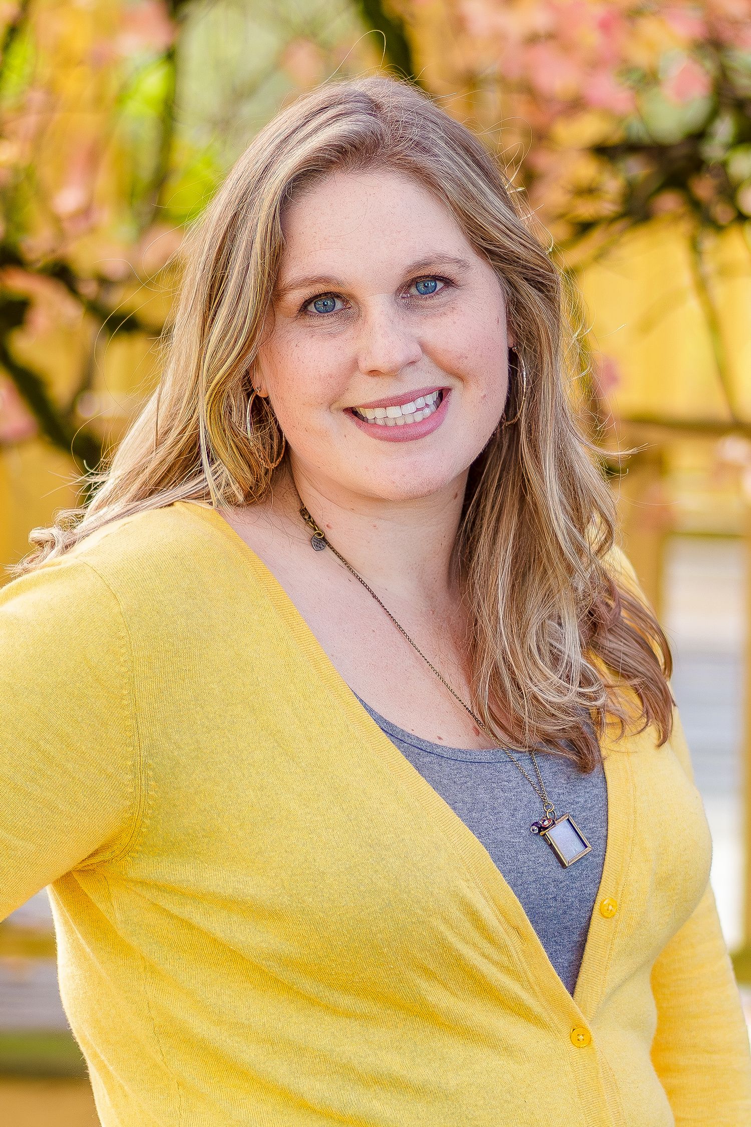 A person wearing a bright yellow cardigan poses outdoors against a blurred autumn background.