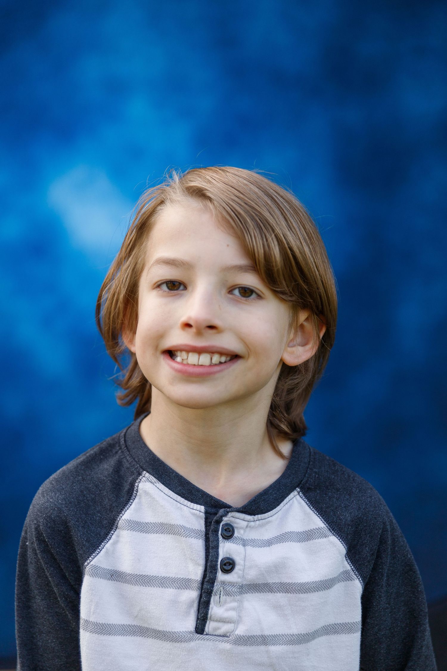 Young person in a striped long-sleeve henley shirt smiles at camera against a blue background.