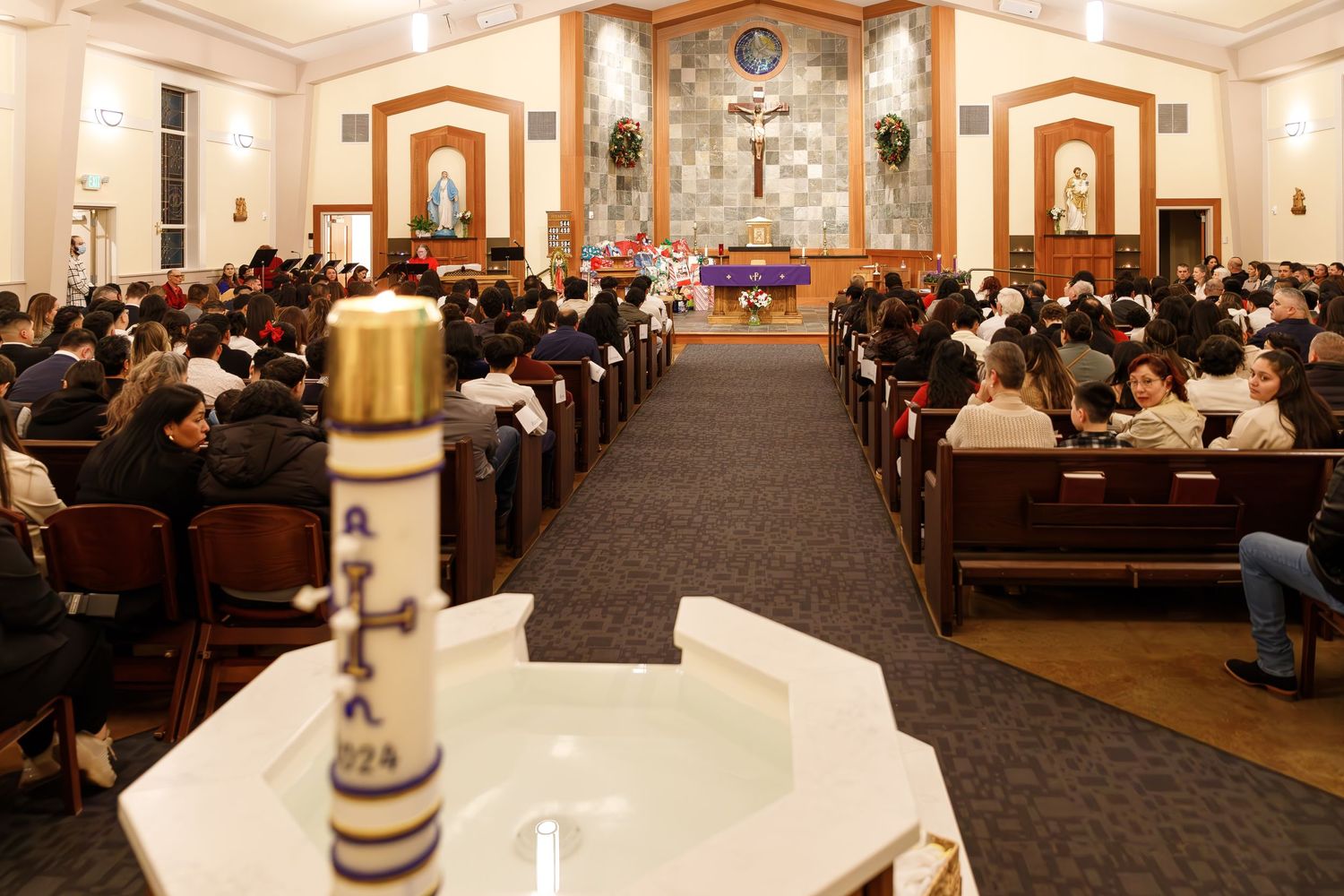 A large congregation fills the pews during a church service with an altar, cross and candles visible at the front.