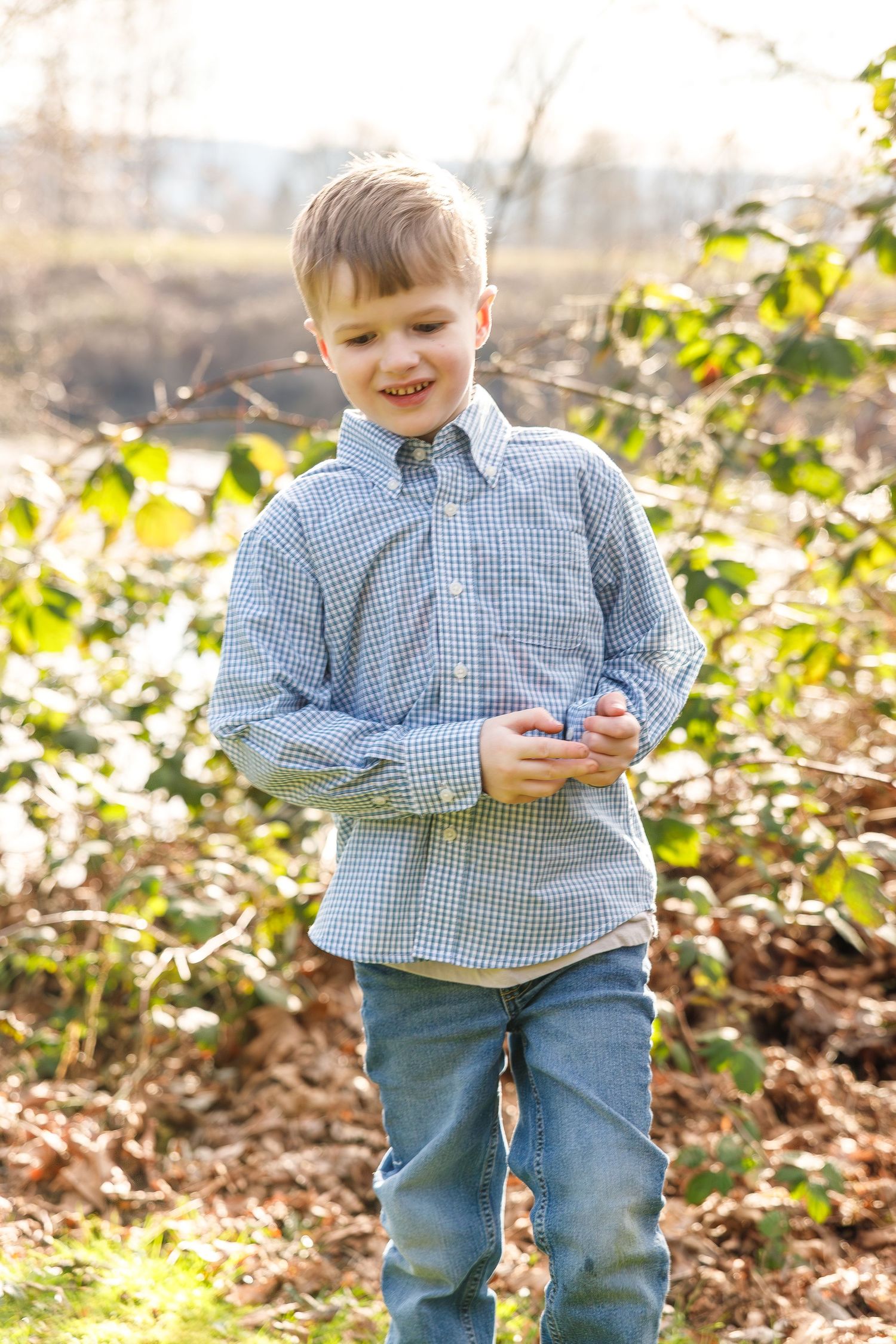 Young child wearing blue gingham shirt and jeans plays outdoors in sunny autumn woods.