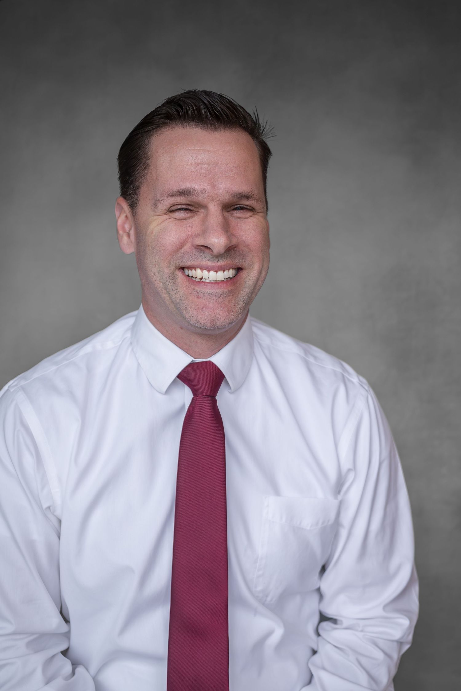 Professional headshot series showing different expressions in white shirt and burgundy tie against gray background.