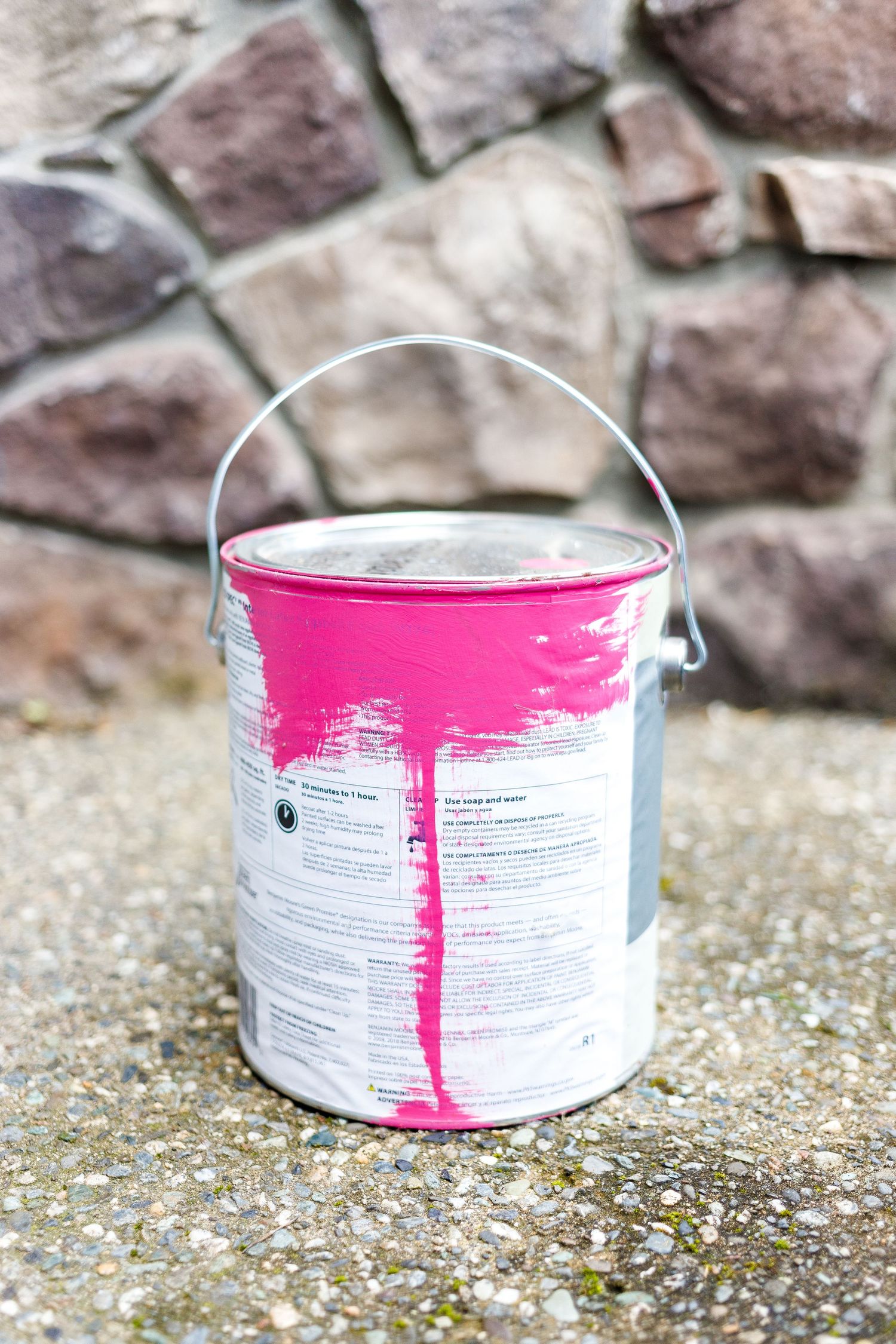 A sequence of pink paint dripping down a white metal paint can against a stone background.