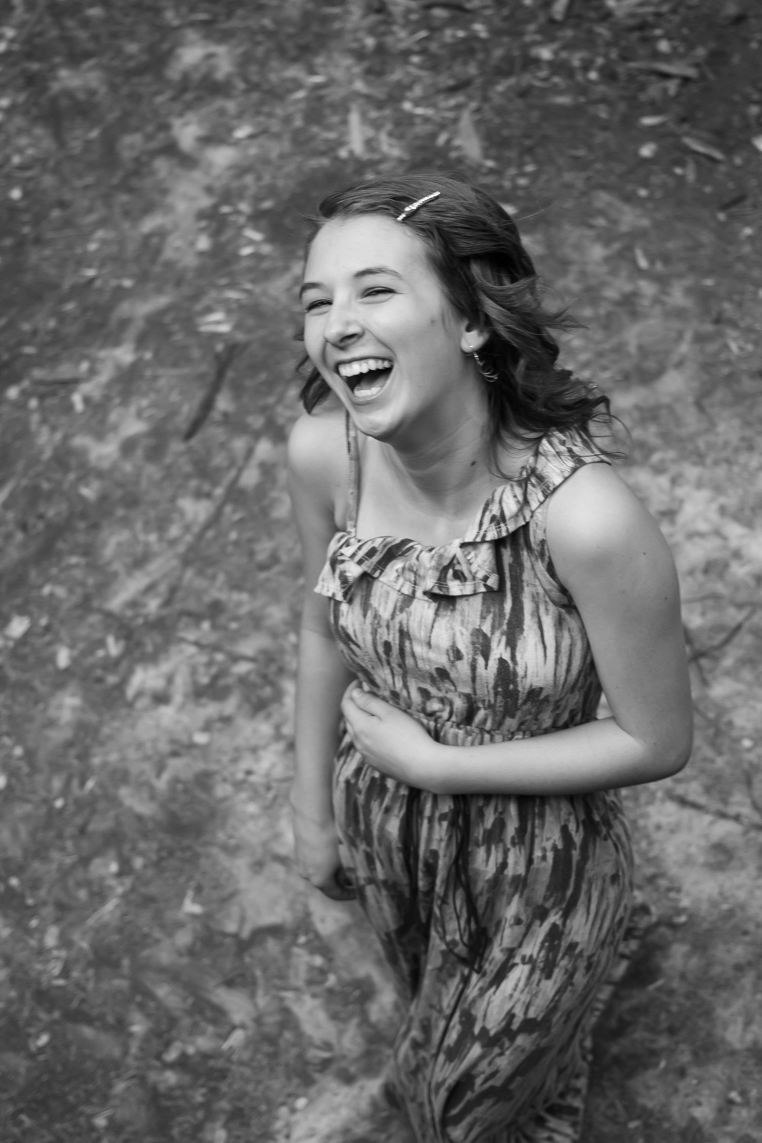 A joyful moment captured in black and white featuring someone wearing a patterned sleeveless dress while laughing outdoors.