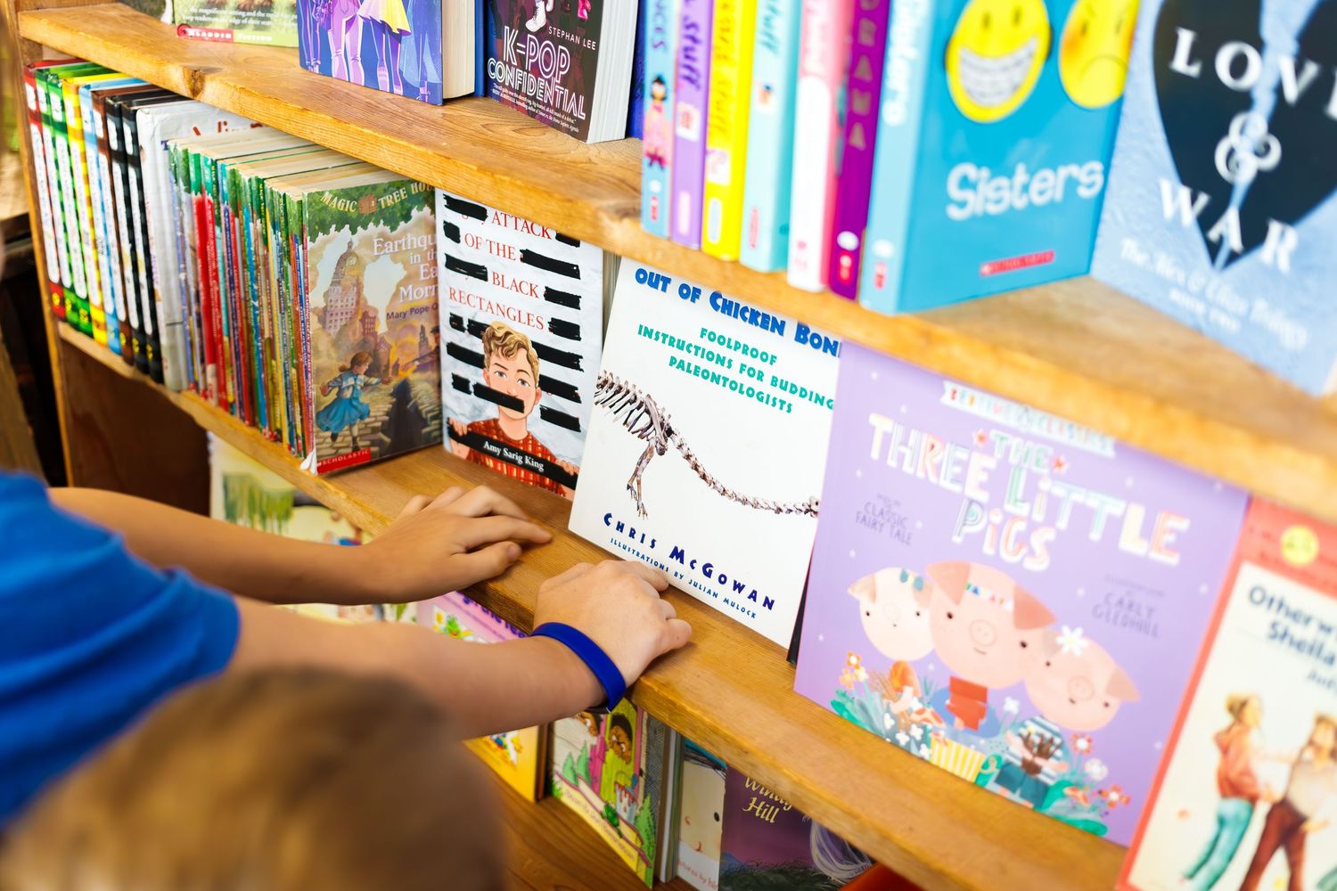 Children's books on wooden library shelves with colorful spines and book covers arranged neatly in a row.