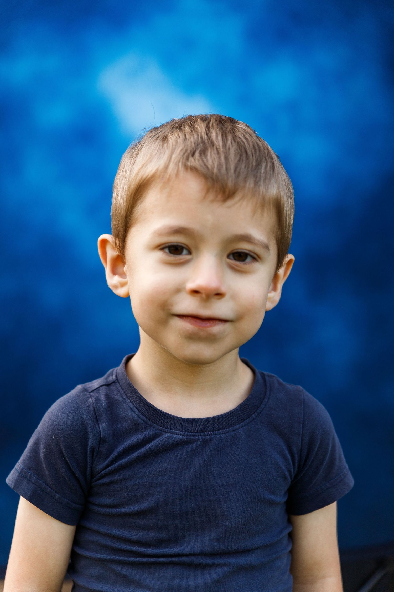 A young child in a navy blue t-shirt poses expressively against a deep blue background.