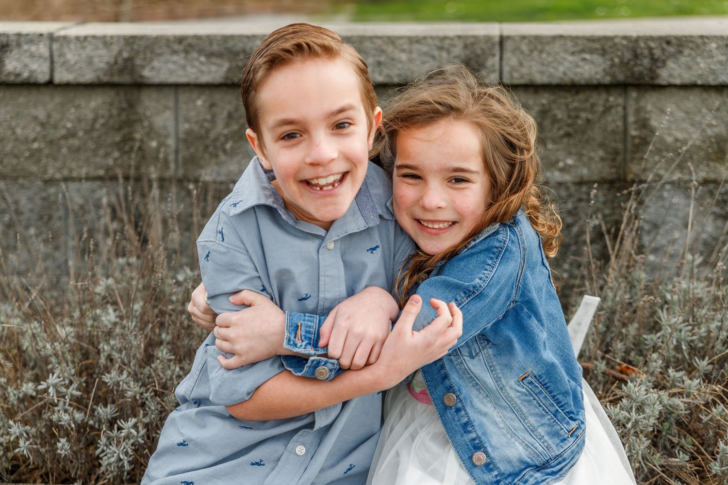 Joyful couple in denim embracing and laughing together against stone wall background.