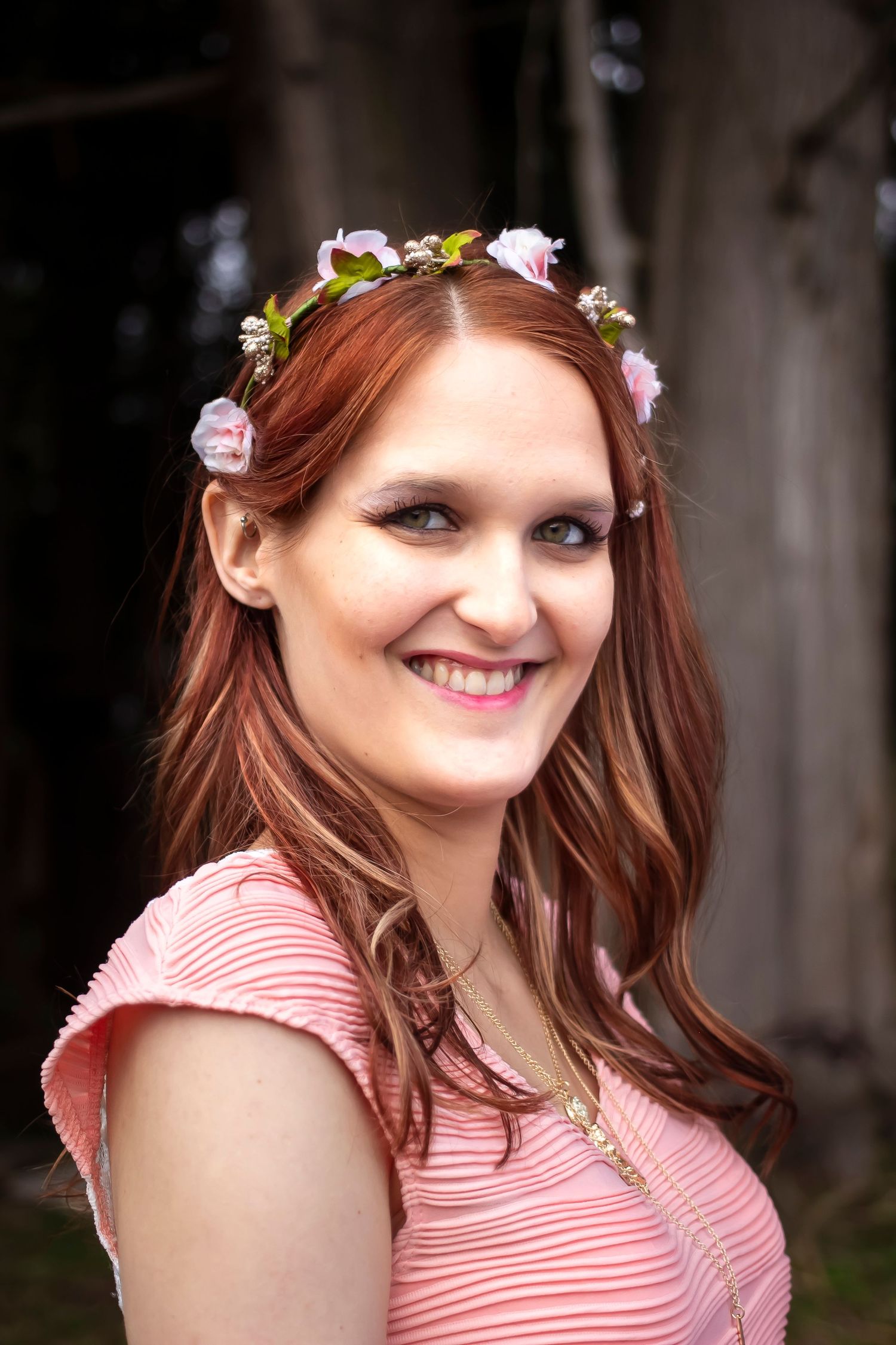 A person wearing a pink and white striped top and floral crown poses outdoors with a cheerful expression.