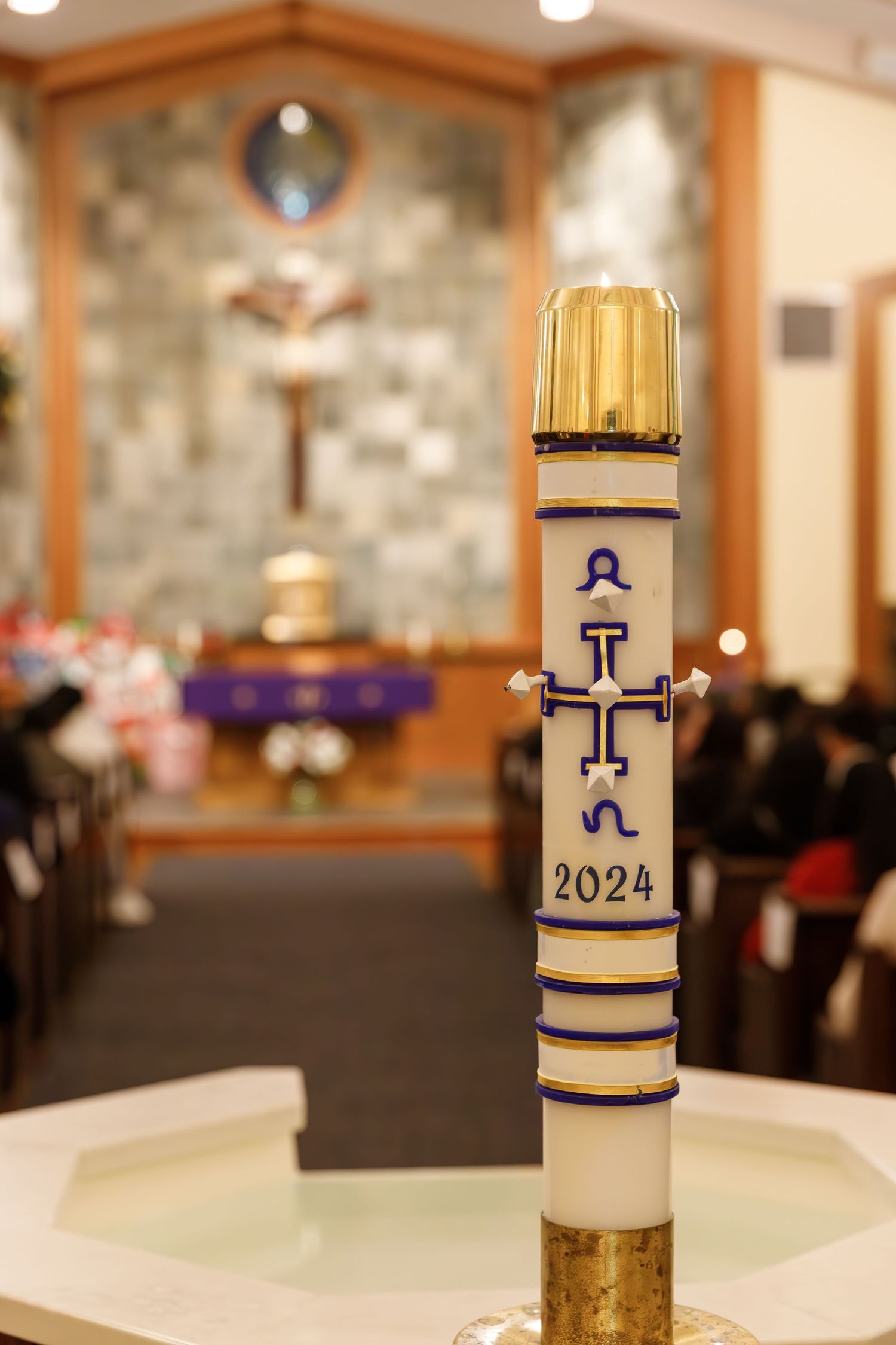 A decorated Easter paschal candle with gold trim and the year 2024 displayed in a church sanctuary setting.