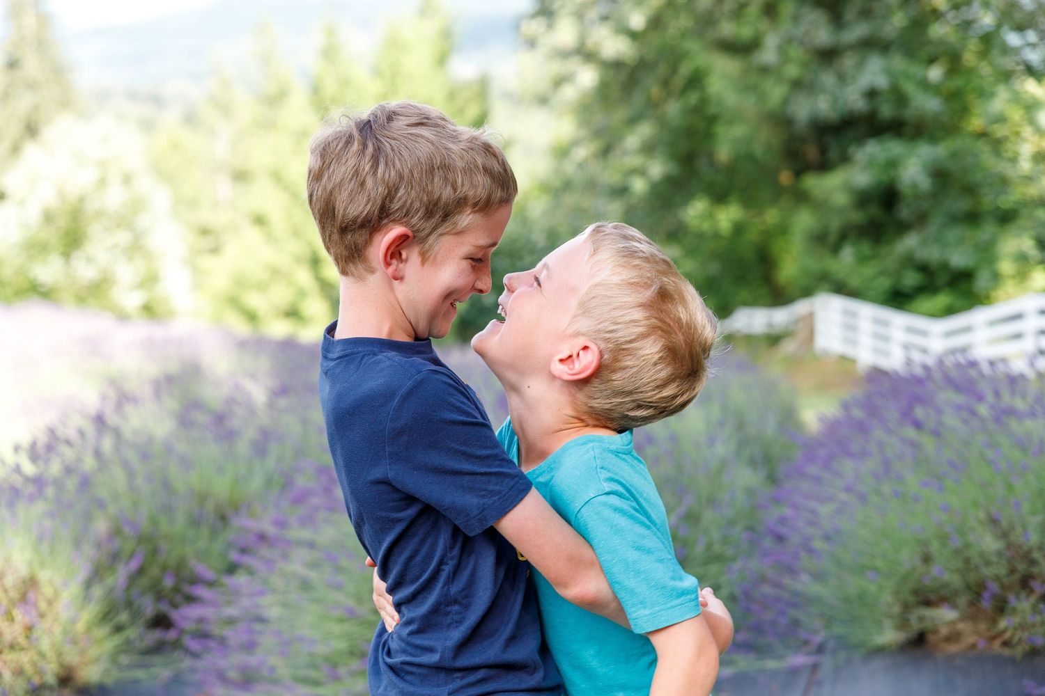 Two children playing and laughing together in a garden with blooming lavender flowers in the background.