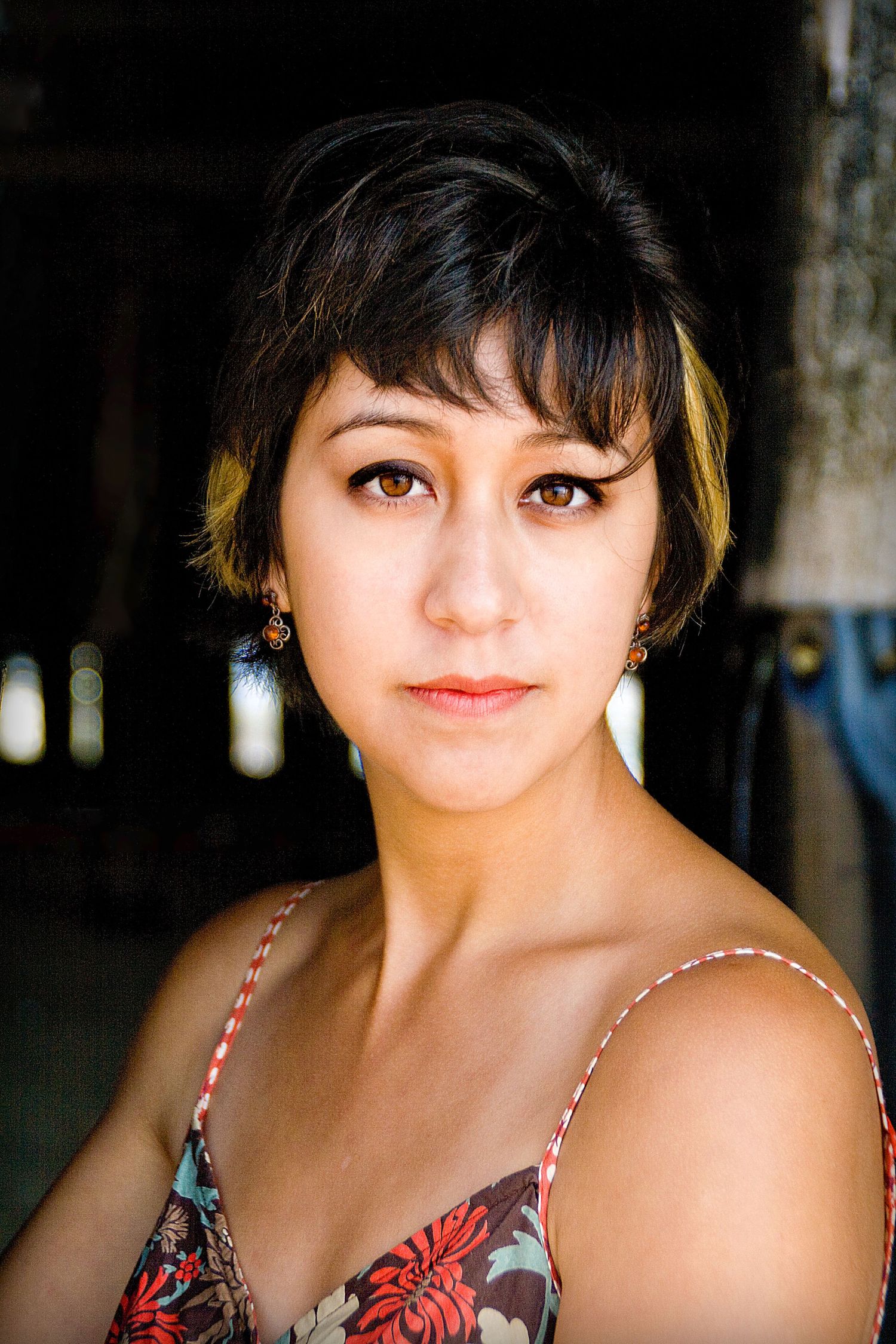 Portrait photo in natural light showing woman with short dark hair wearing floral print top with delicate earrings.