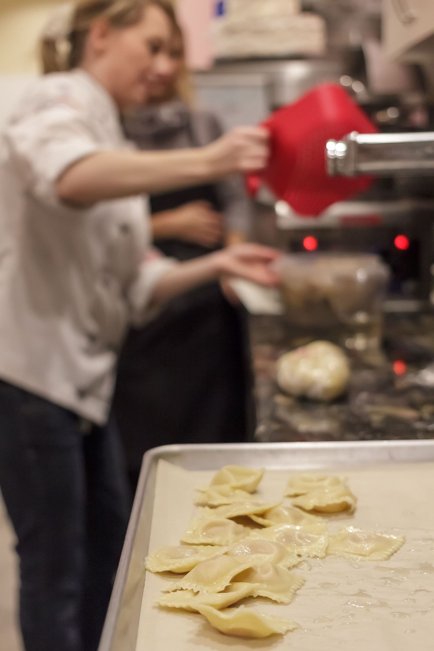 Fresh homemade ravioli pasta laid out on wooden cutting board in restaurant kitchen with chef working in background.