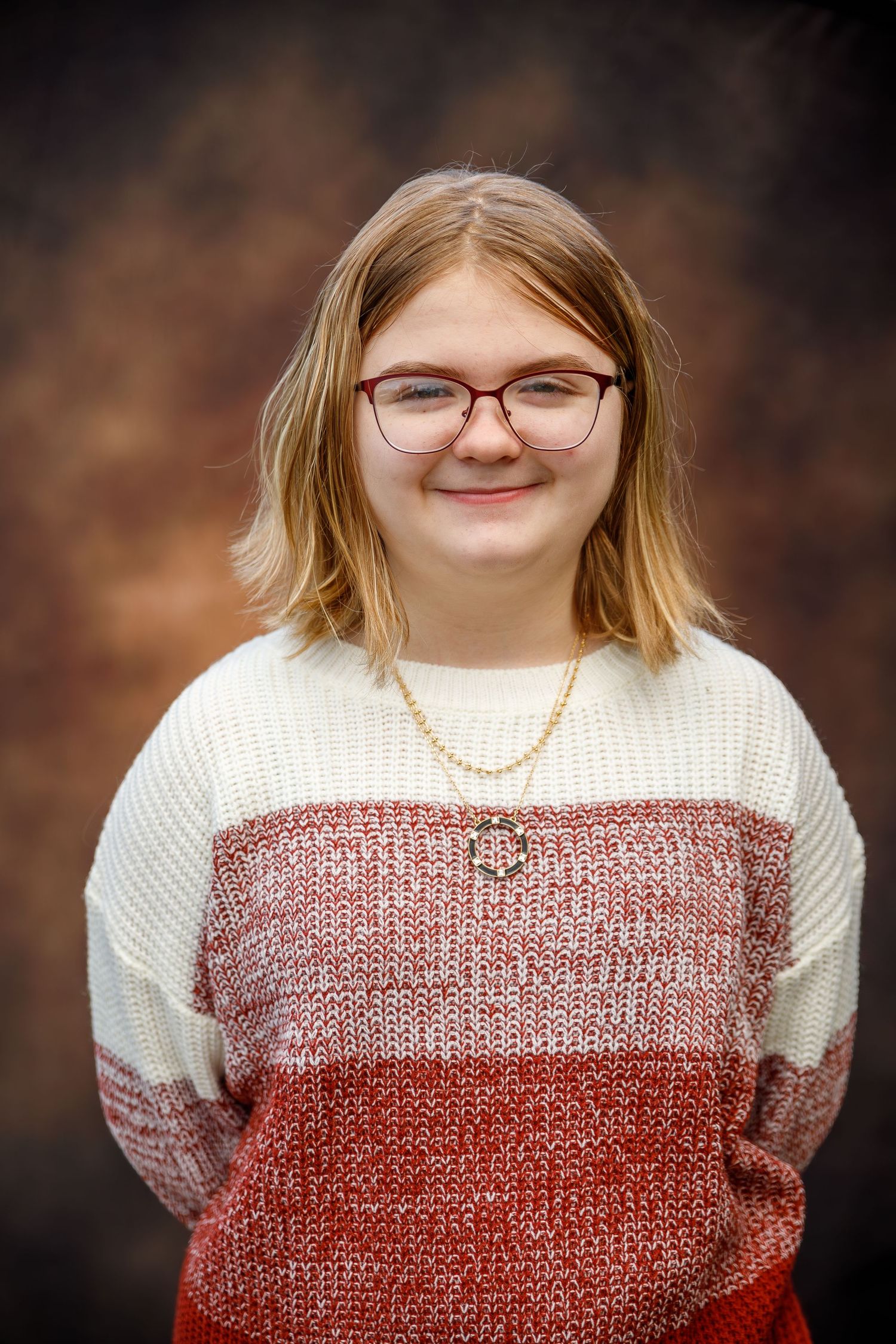 Portrait of someone wearing glasses and a cozy color-block sweater in cream and rust tones against a dark background.