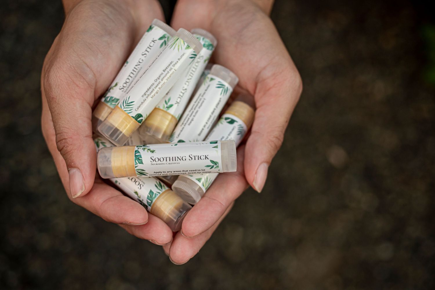 Cupped hands holding multiple small glass vials with light-colored labels against a dark background.
