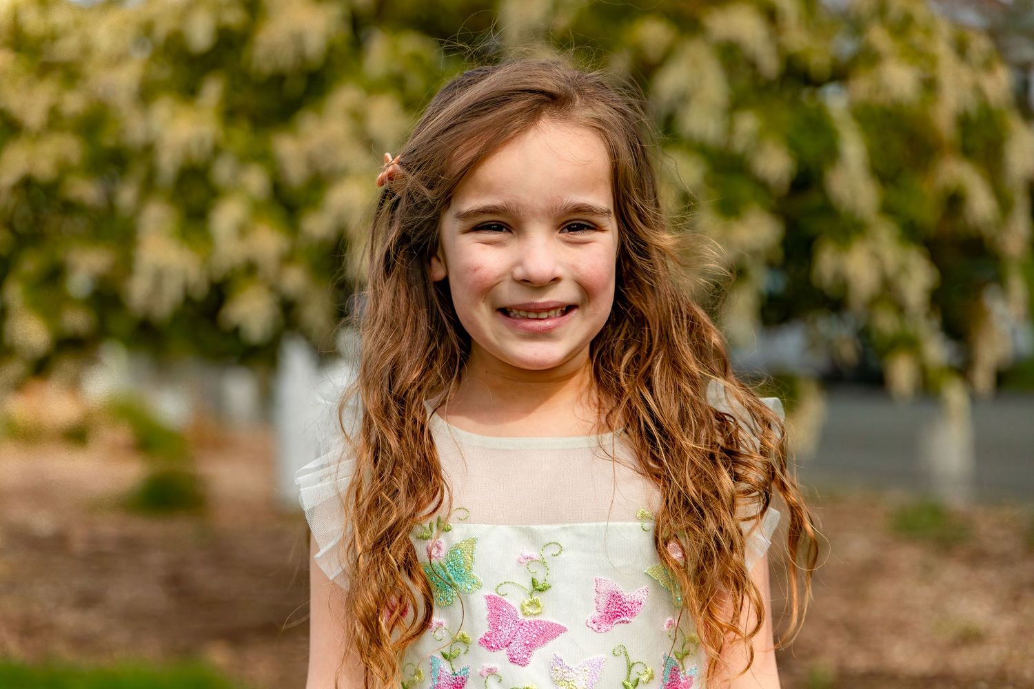 A child in a floral dress smiles while posing outdoors against a blurred green background.
