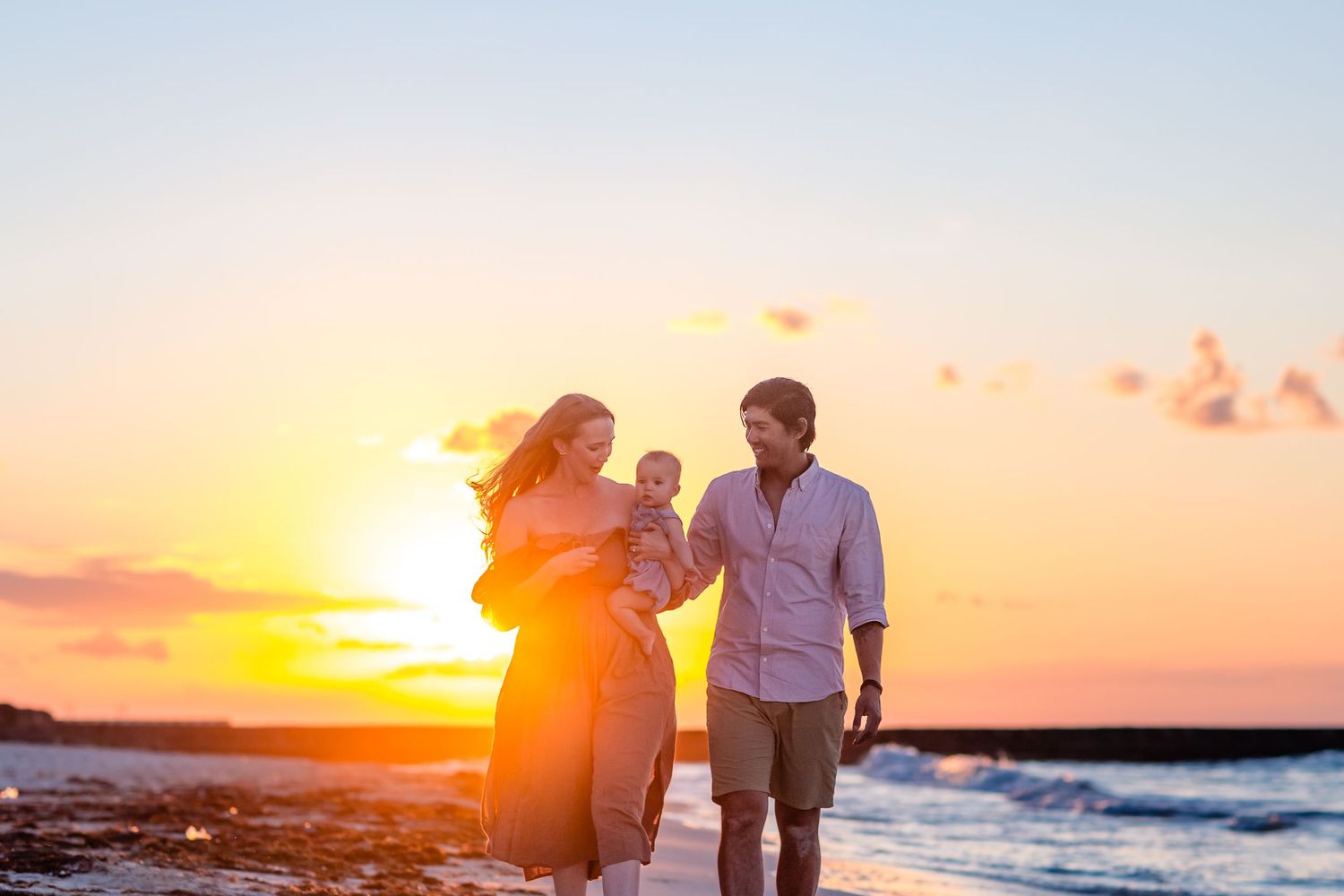 Family walking on Cozumel beach at sunset during photoshoot, golden sky reflecting on ocean waves.