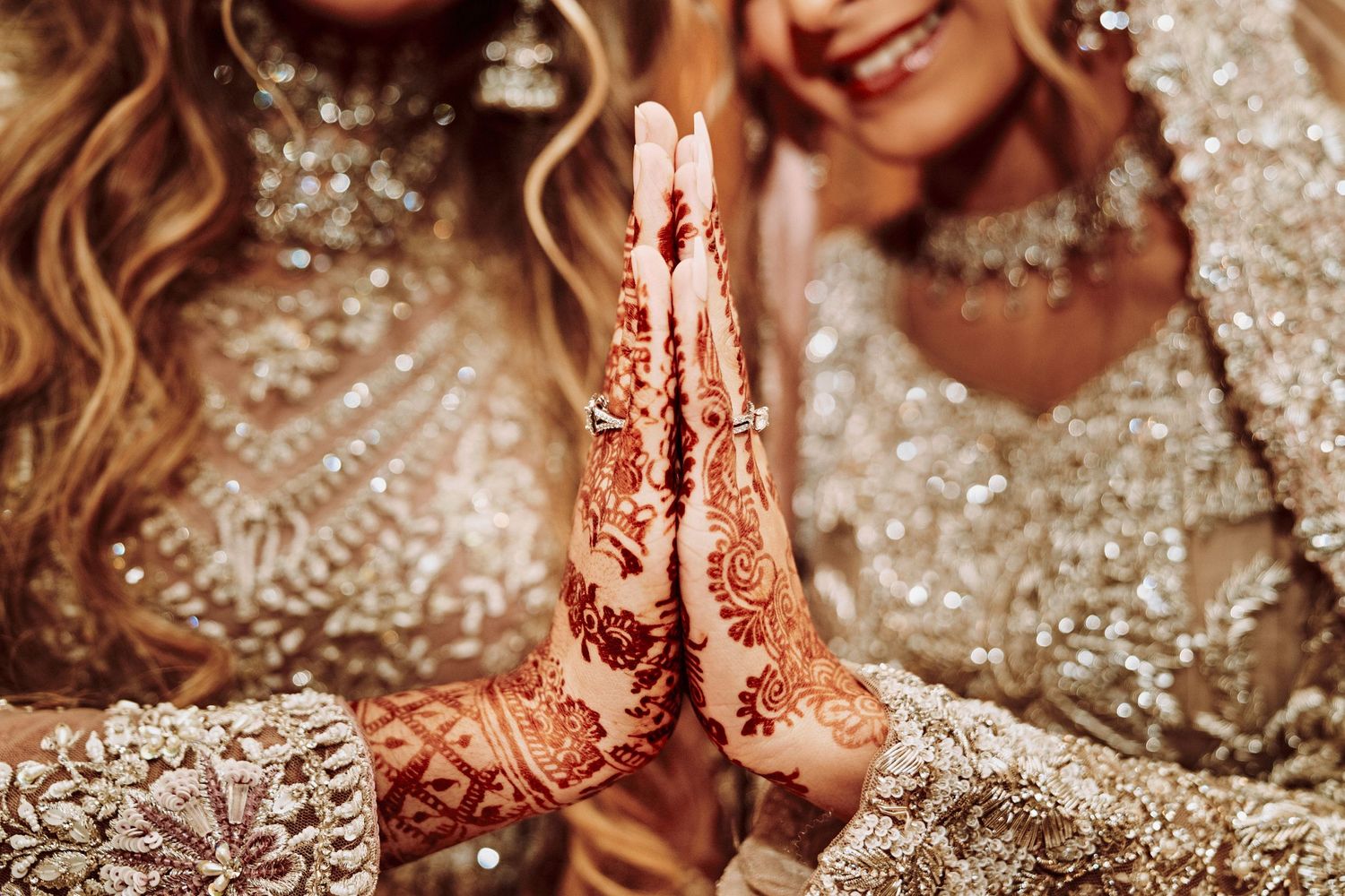 Intricate henna design on hands with sparkly traditional wedding attire in the background.