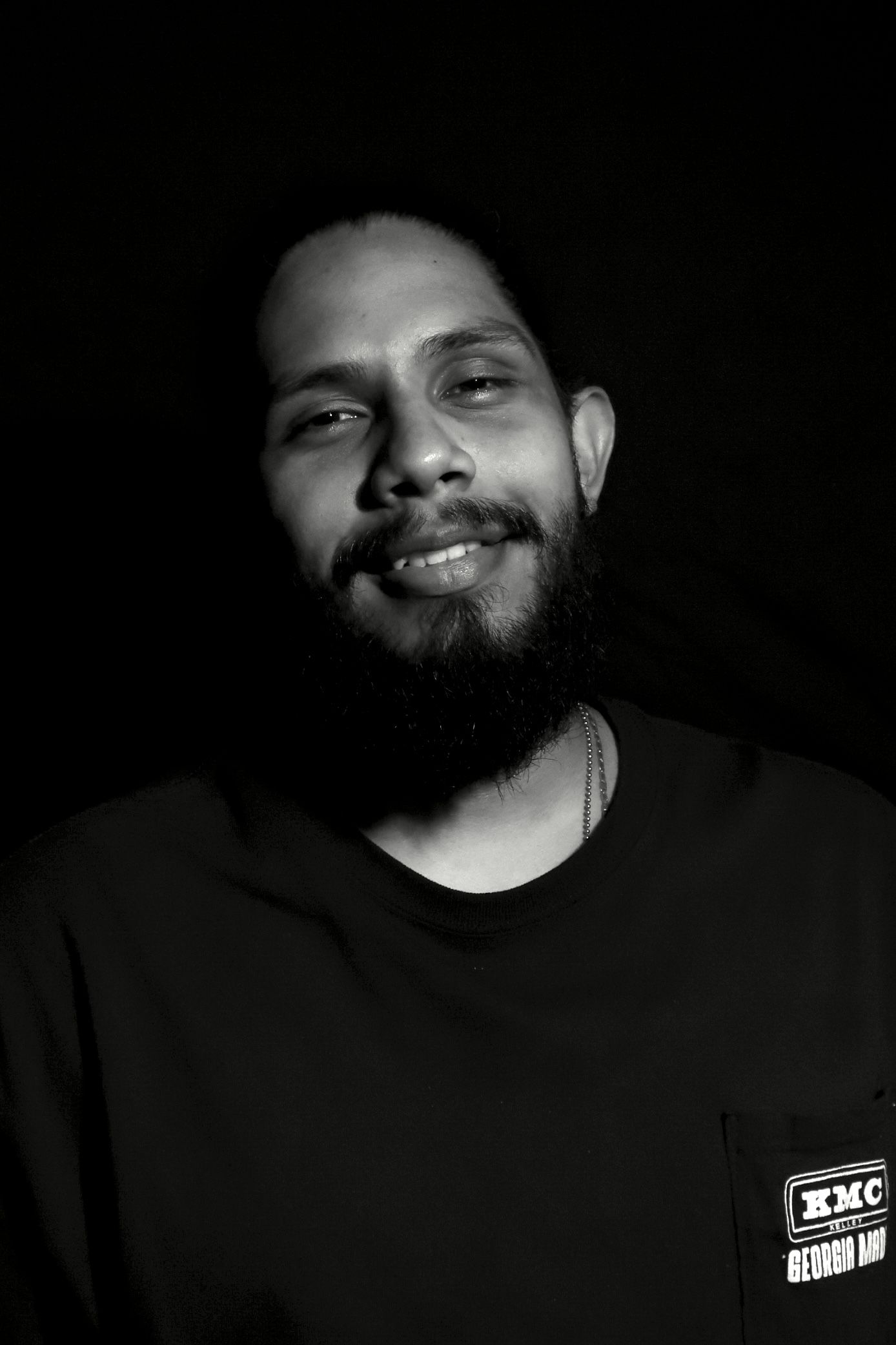Black and white portrait with genuine smile wearing casual dark clothing.