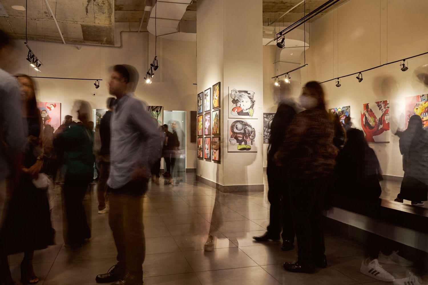 People browse artwork in a modern gallery space with track lighting and displayed pieces on walls.