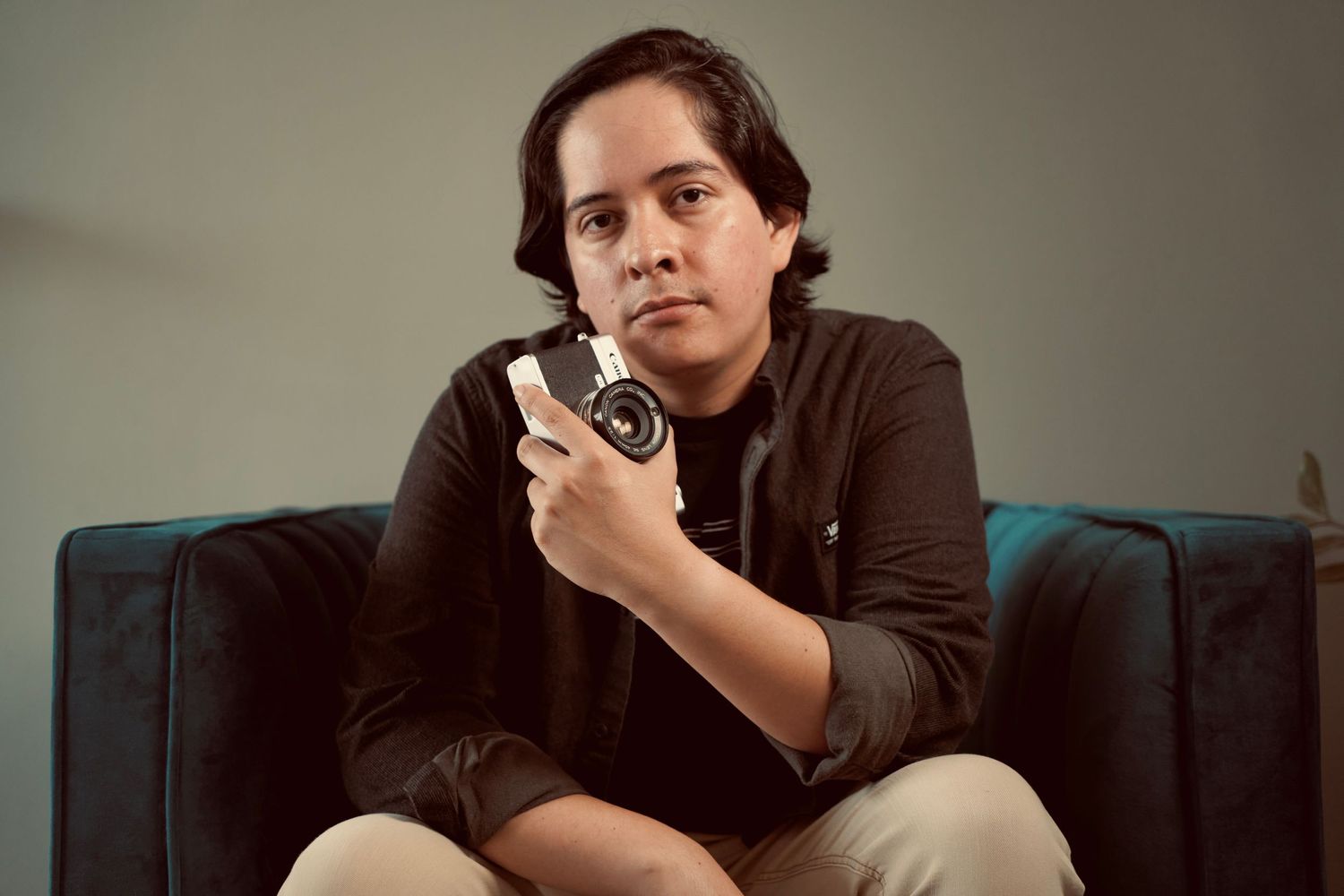 A photographer sits on a blue couch holding a vintage camera.
