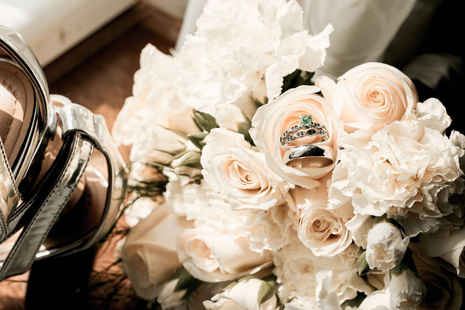 Wedding rings nestled among delicate blush pink roses and white flowers in a bridal bouquet.