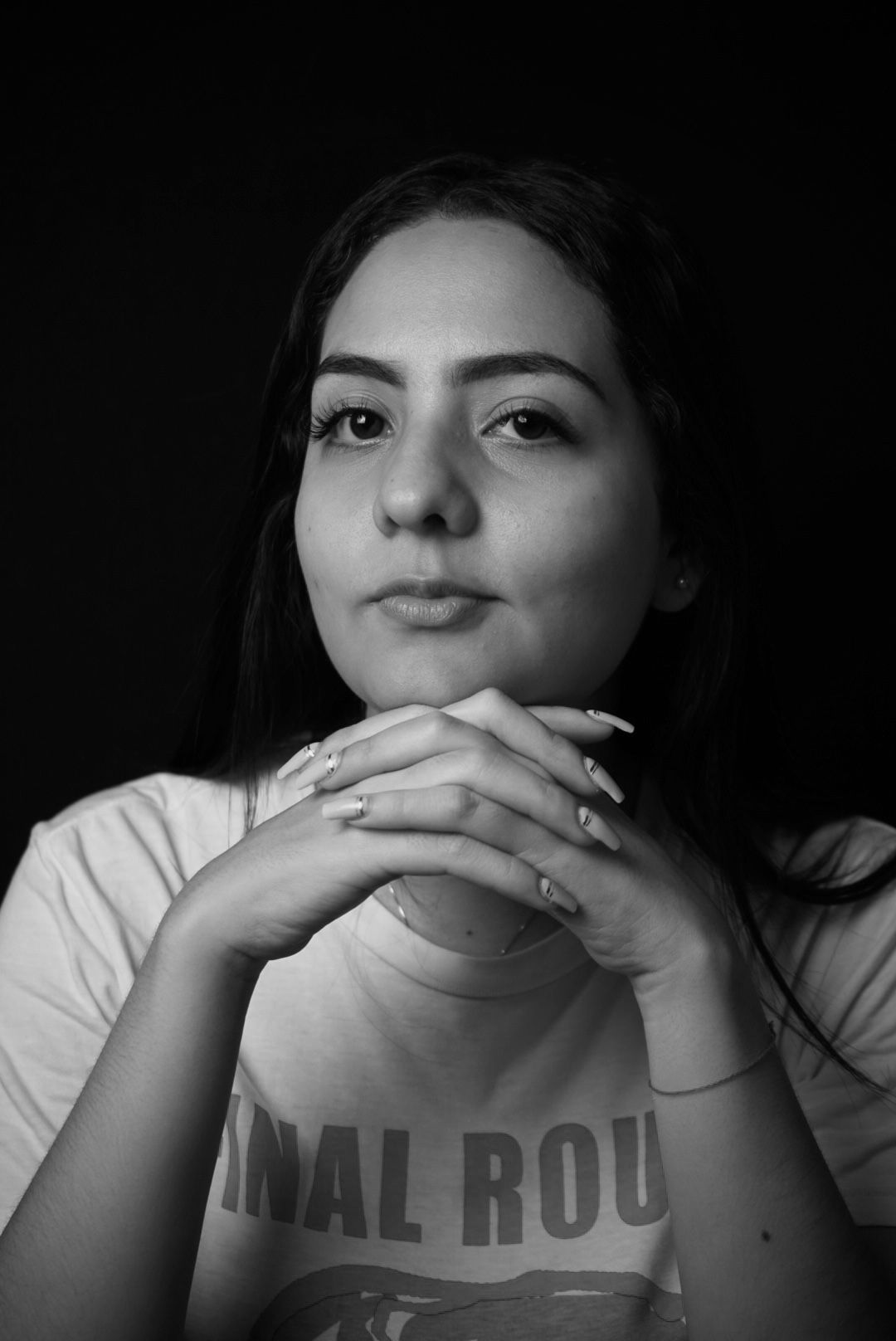 Black and white studio portrait with clasped hands and casual attire.
