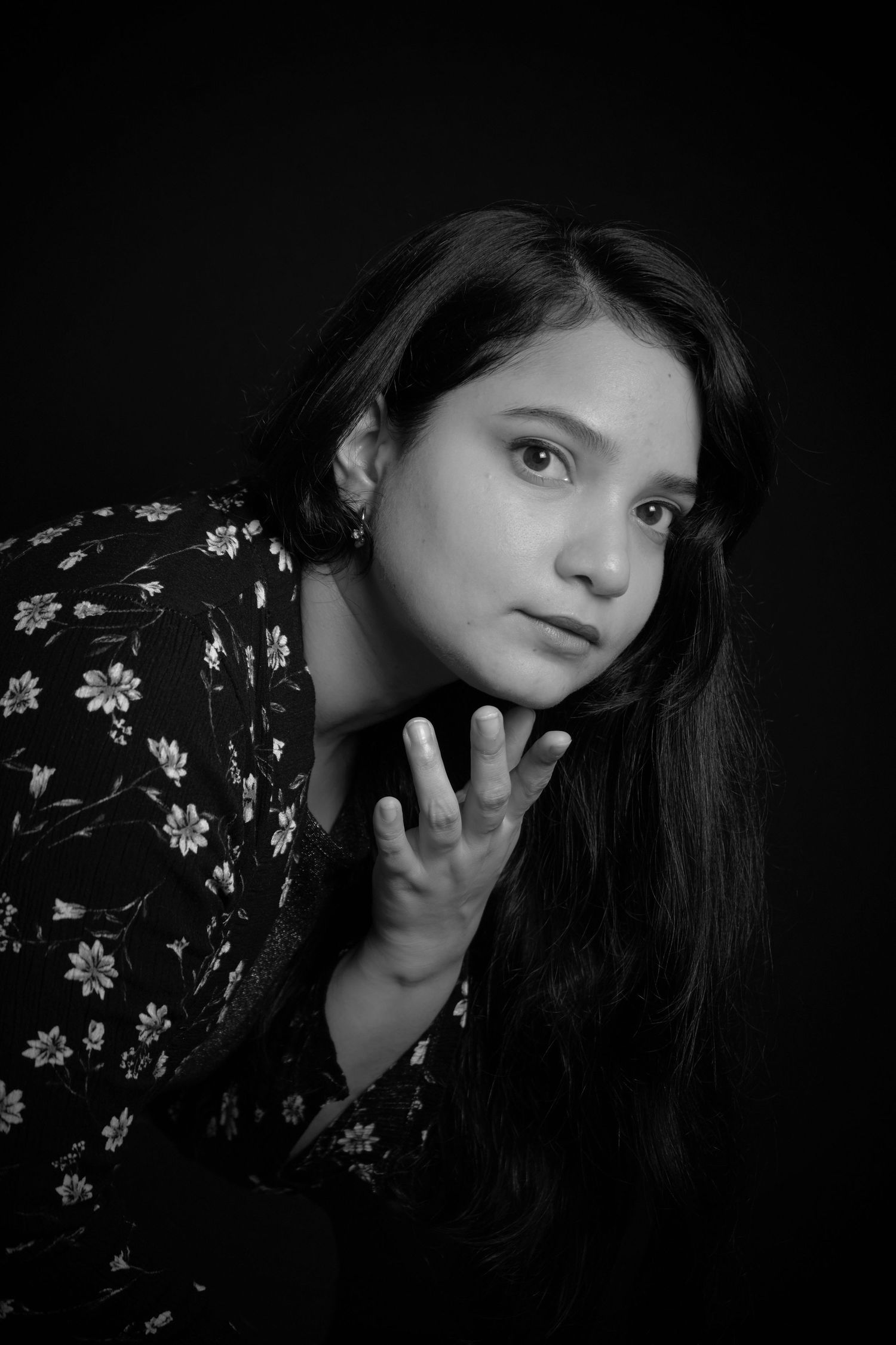 Black and white portrait of someone in a floral dress against dark background.