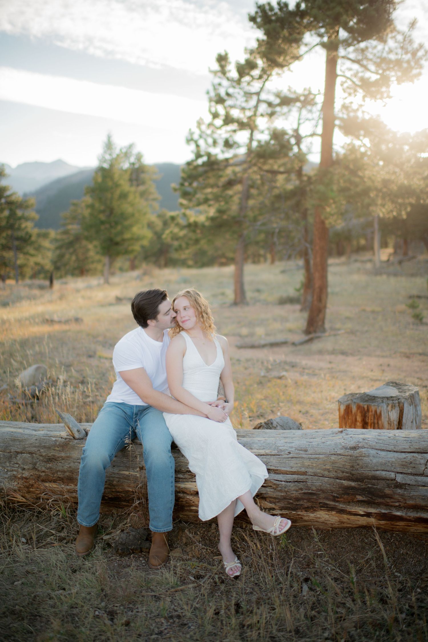 Couple sitting together on fallen log in mountain forest during golden sunset hour.