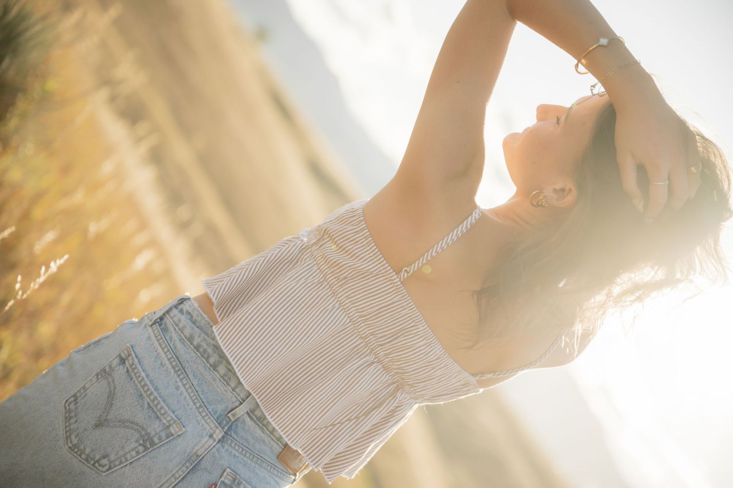 A person in denim shorts and white top stands in golden sunlight creating a dreamy backlit silhouette effect.