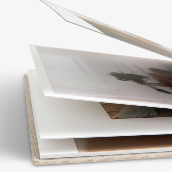 Close-up view of a layered photo album with white pages fanned open showing printed photographs inside.