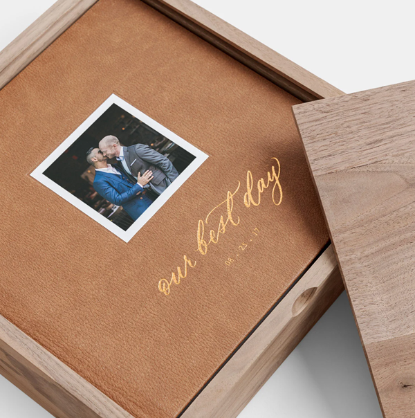 A brown leather photo album or portfolio with gold lettering lies on a wooden surface.