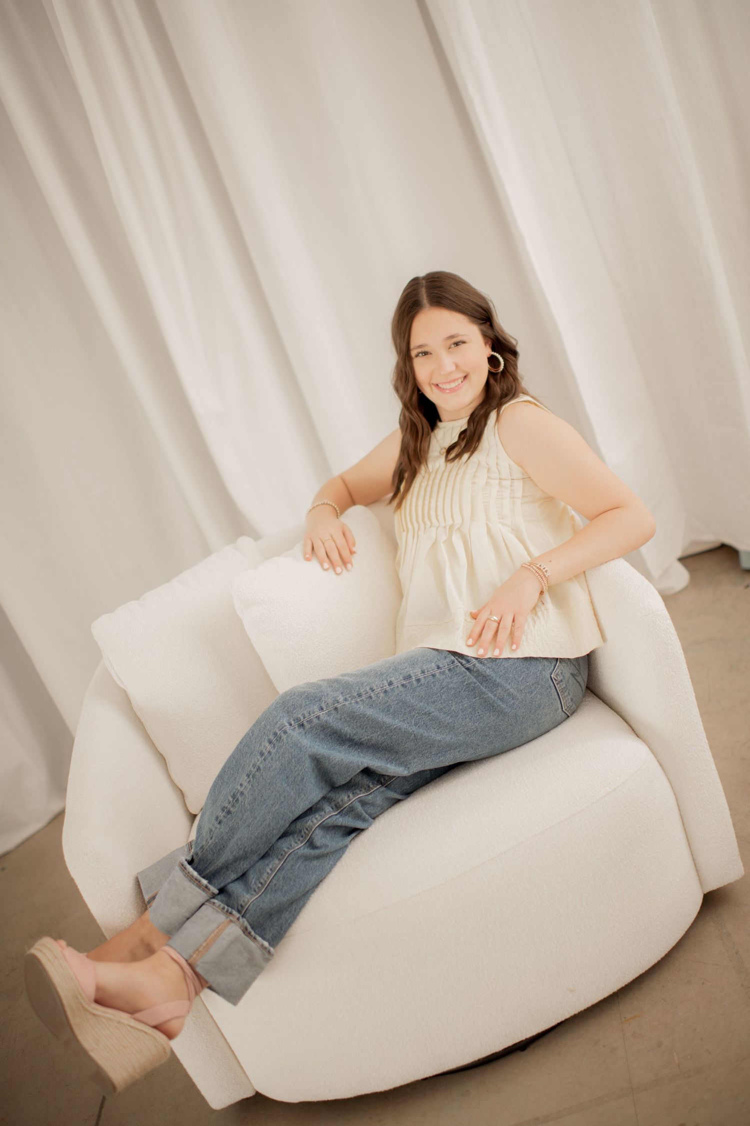 A woman in jeans lounges comfortably on a white bean bag chair in a minimalist studio setting.