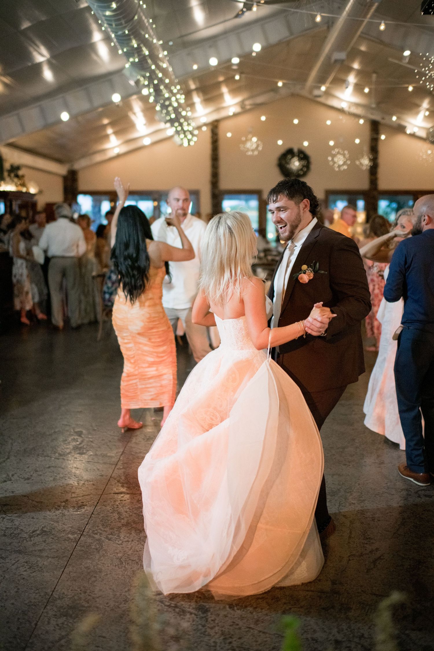 Wedding party members dance and twirl in flowing dresses during a reception celebration under twinkling lights.