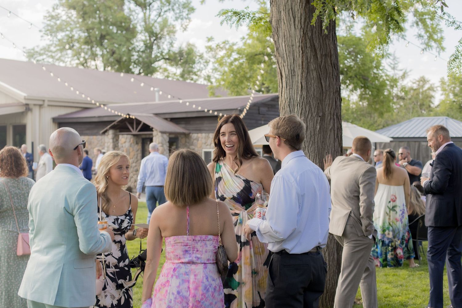 Wedding guests gather under a canopy tent for an outdoor celebration in a natural setting.