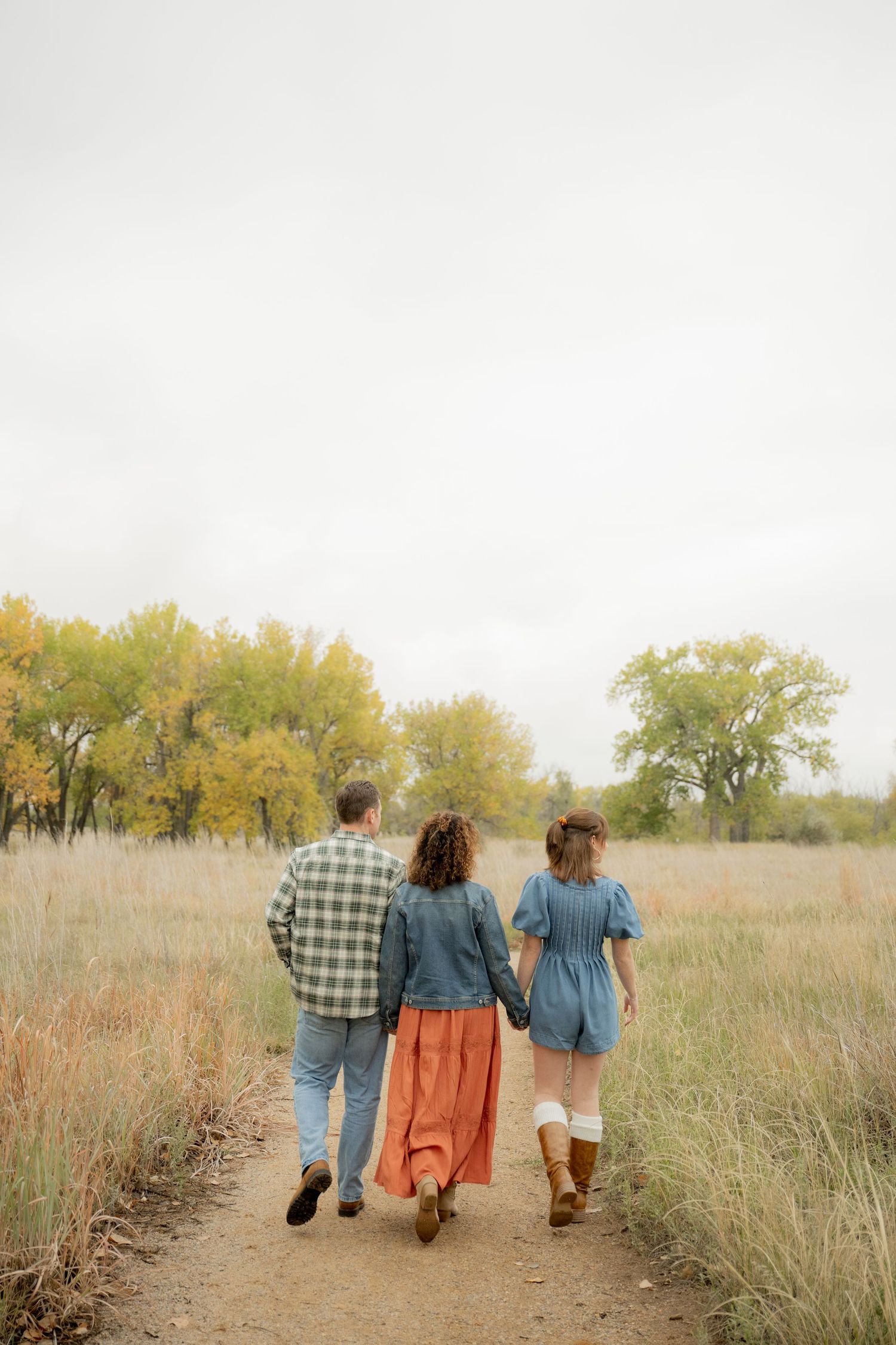 Three people walking together on a path through autumn grassland wearing casual denim and plaid clothing.