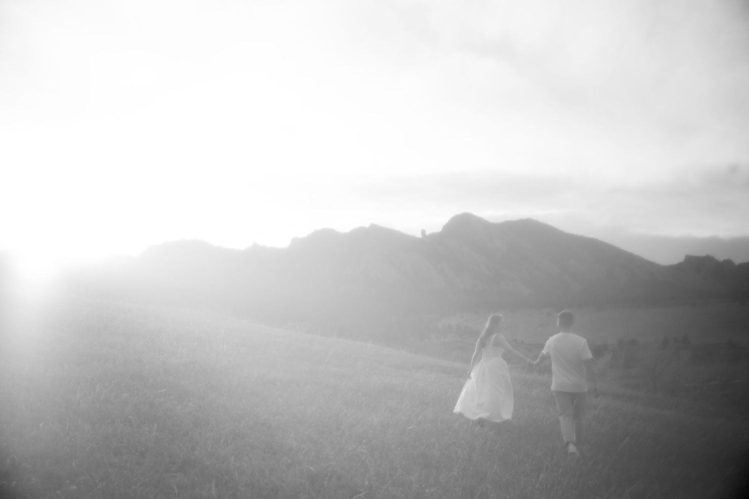 Two silhouetted figures walking through a misty mountain landscape at sunset with soft diffused light.