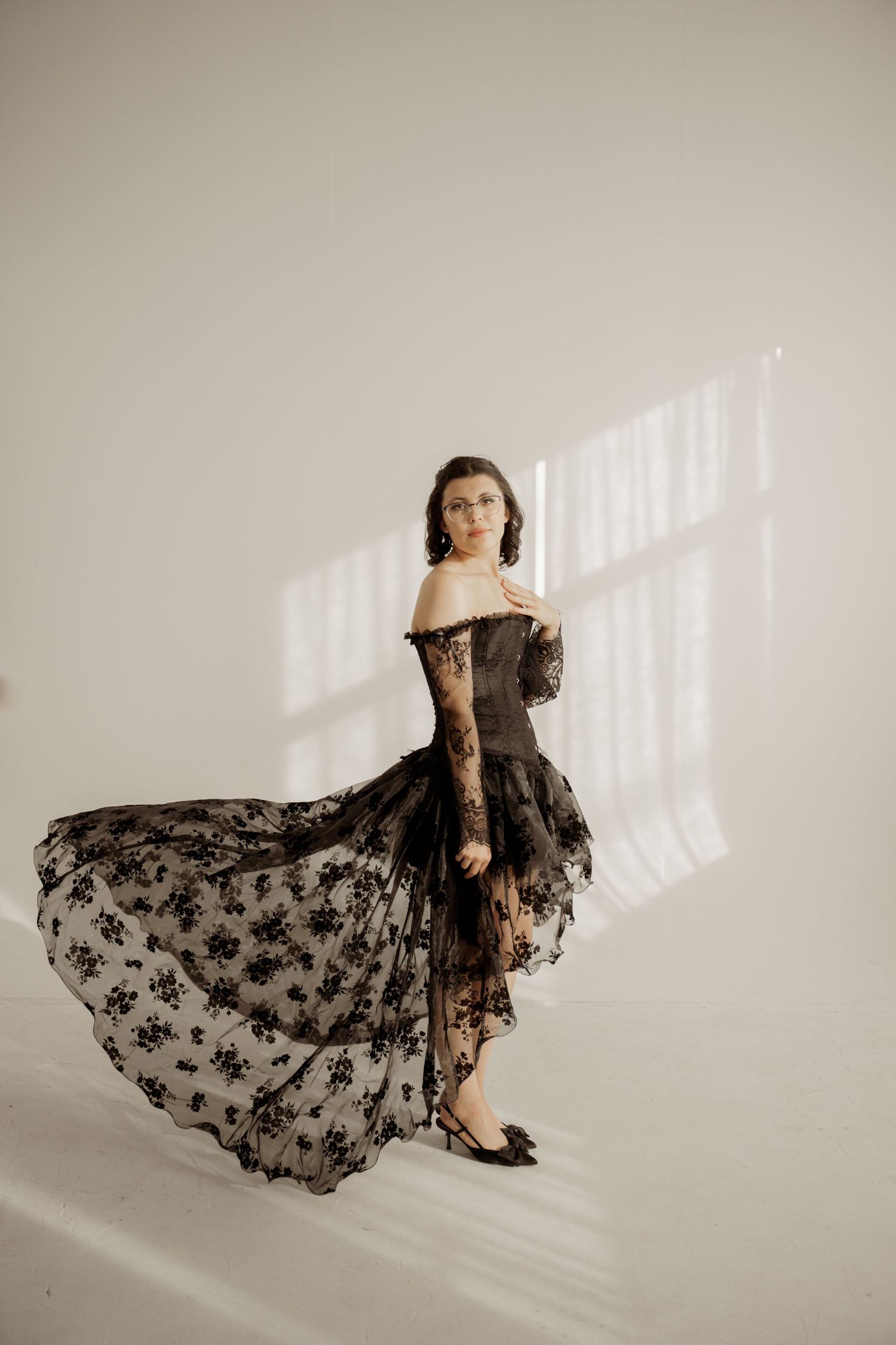 Elegant black lace dress with flowing skirt photographed in minimalist setting with dramatic window lighting.