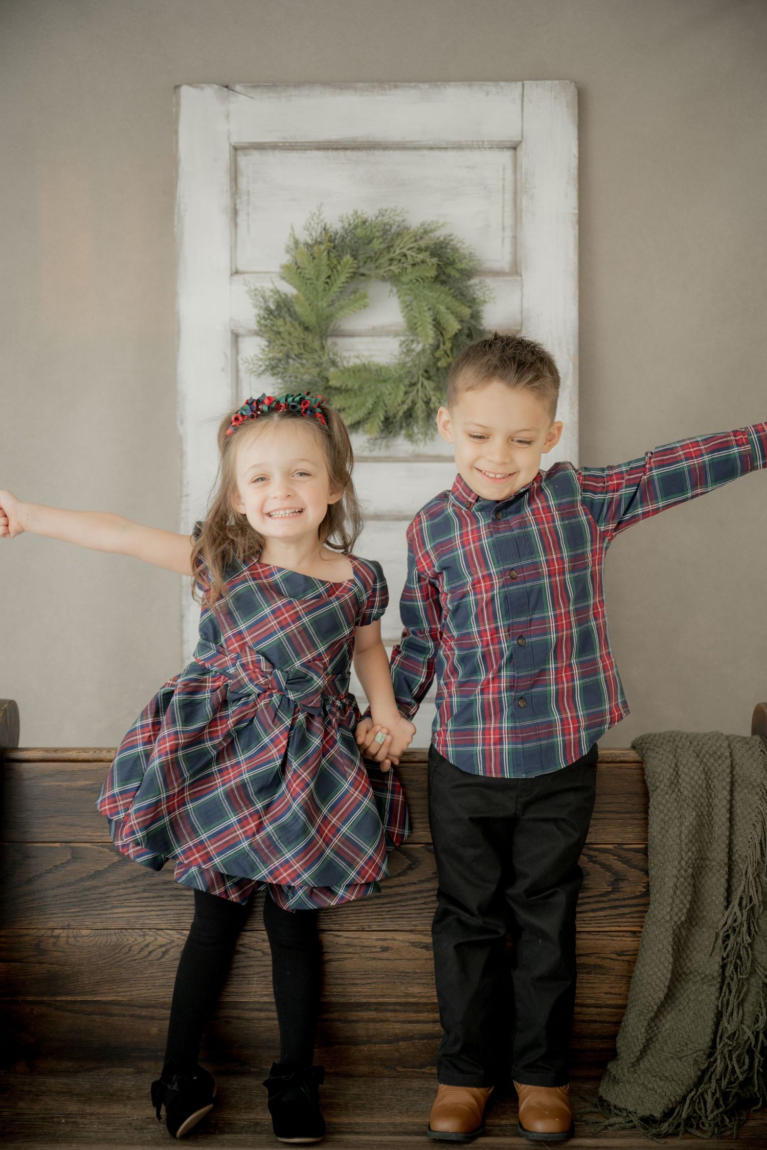 Two children in matching plaid shirts playfully lean against each other in a series of candid poses against a gray wall.