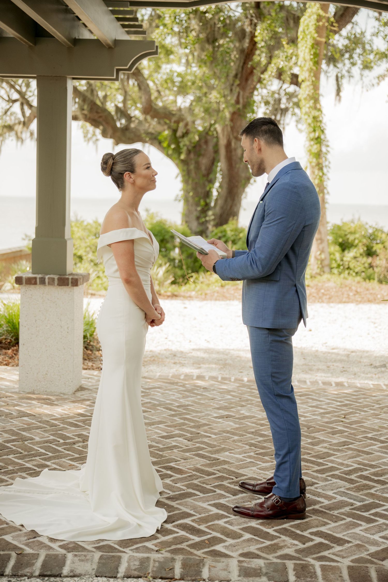 A bride and groom share an intimate moment during their first look on a brick patio surrounded by Spanish moss trees.